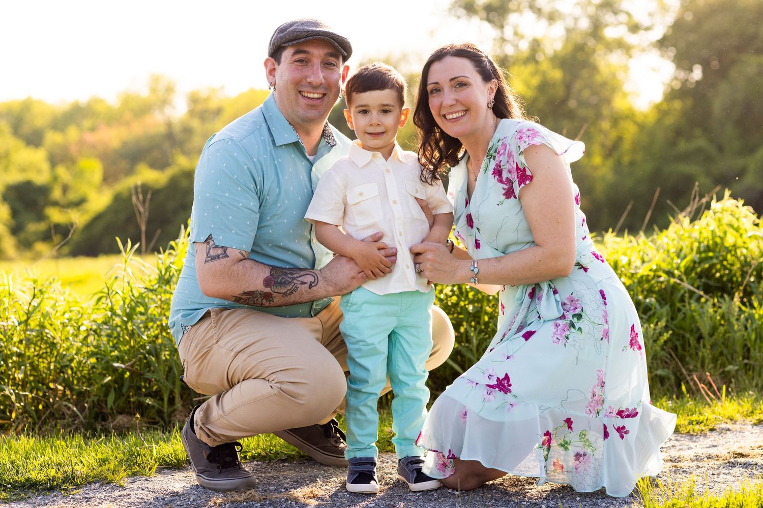 Happy family portrait with parents and toddler son outdoors in golden hour sunlight among lush greenery.