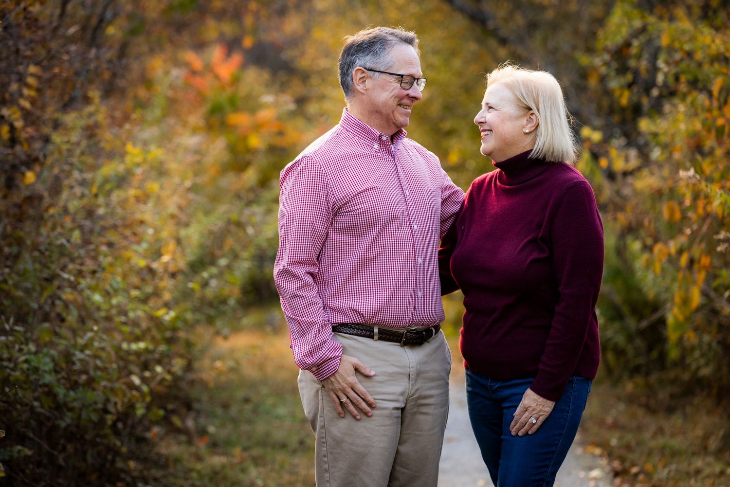 Happy couple gazing at each other on a scenic fall nature path surrounded by colorful foliage.