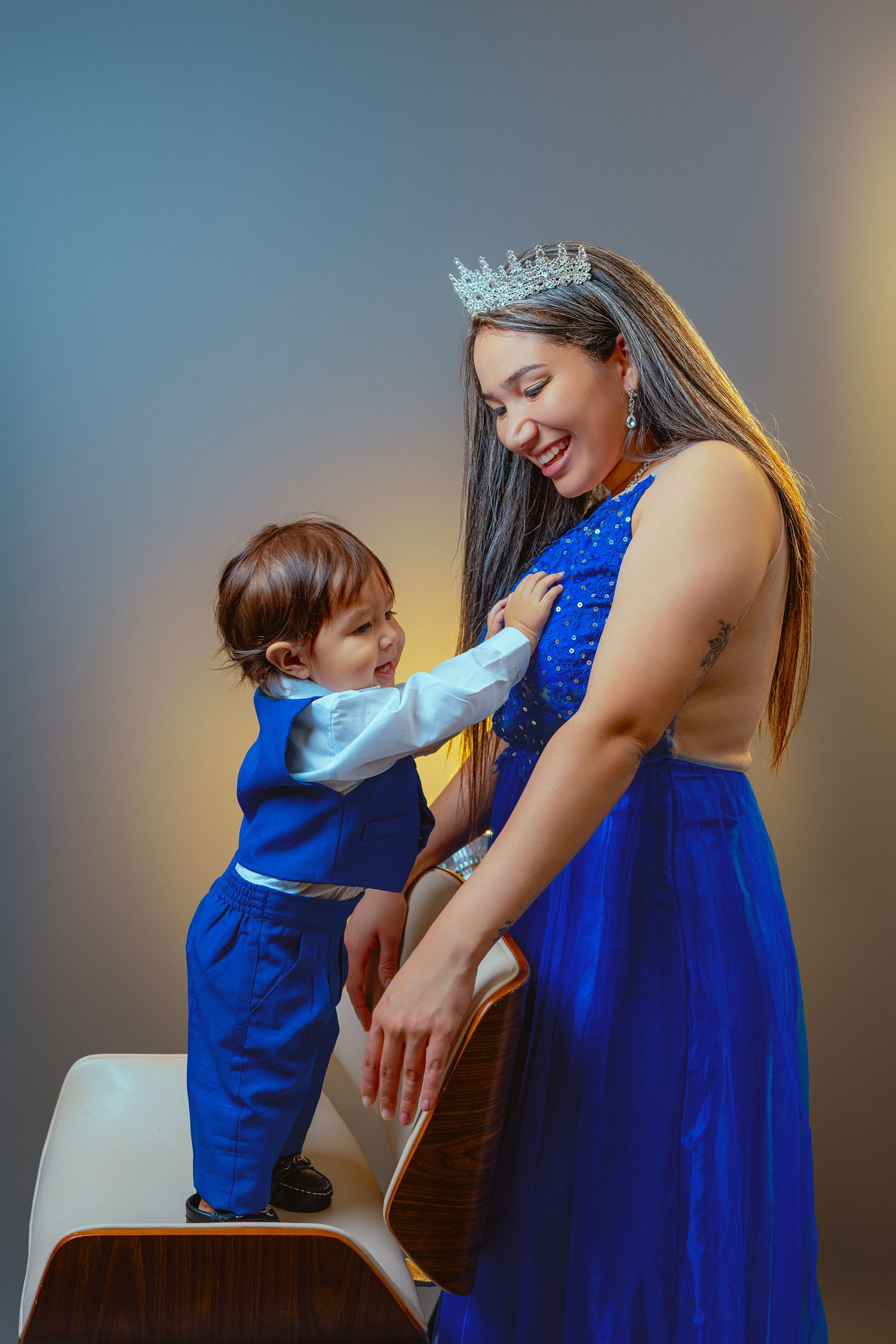 A touching moment captured in blue formal wear with a tiara against a studio backdrop.