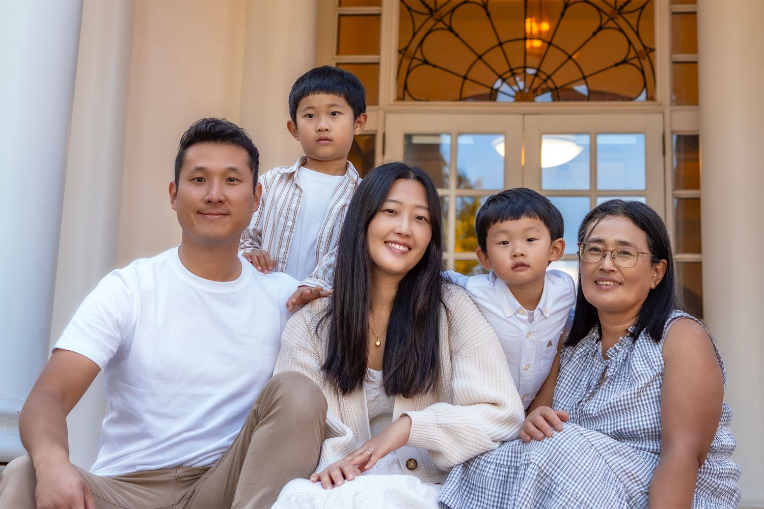 Happy Asian family of five posing together on steps outside an elegant building for a portrait photo.