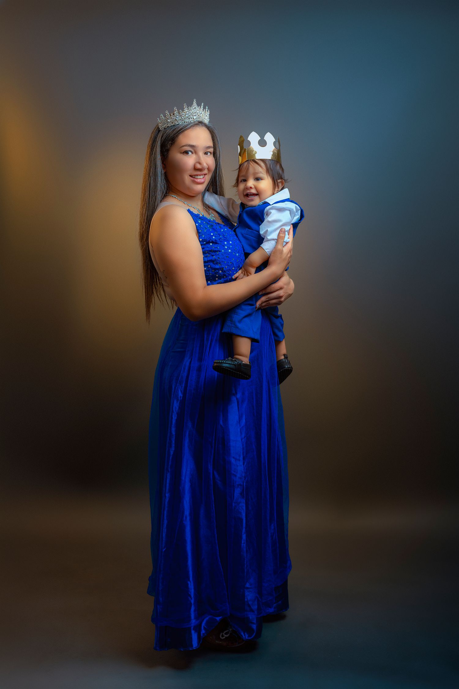Mother and child wearing matching royal blue dresses pose together for a portrait series against dark background.