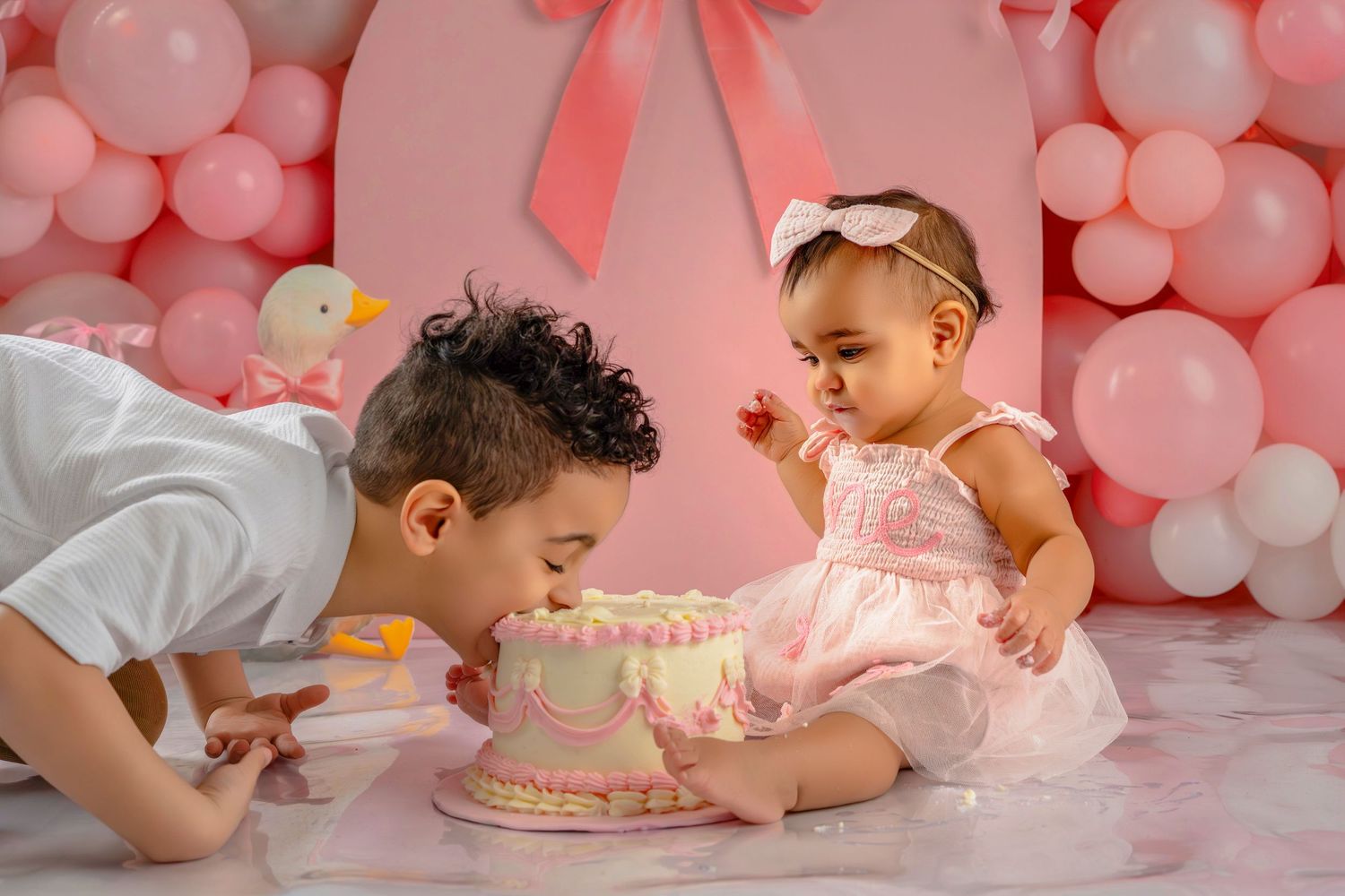 A baby in pink smashes their face into a pink birthday cake during a cake smash photo session.