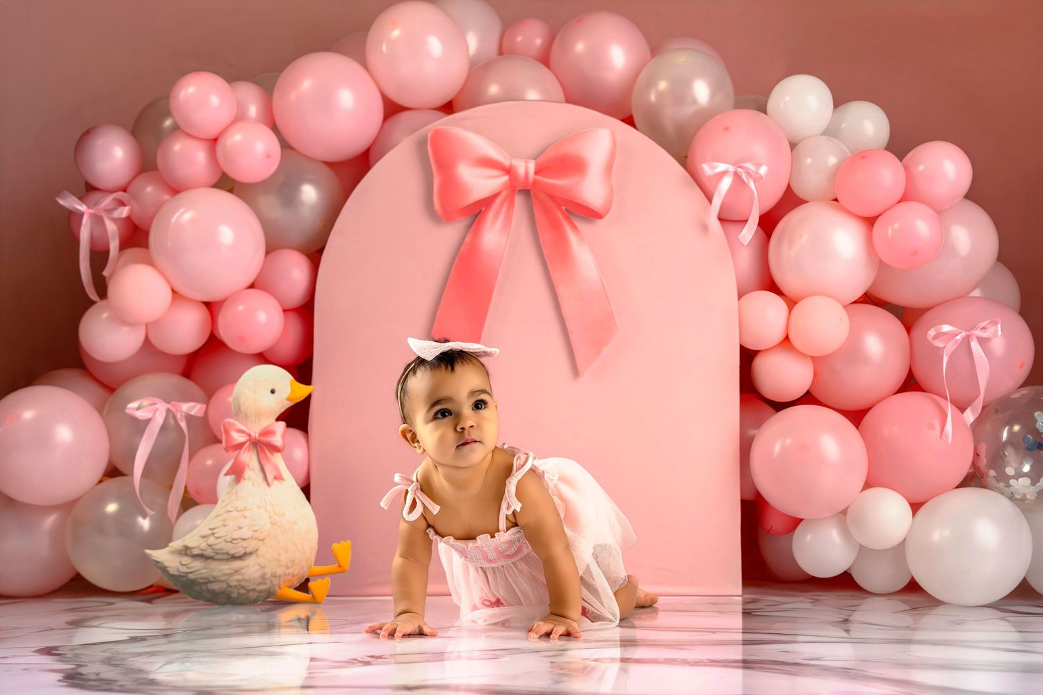 Pink balloon garland and decorative setup for a baby's first birthday cake smash photo session with soft lighting.