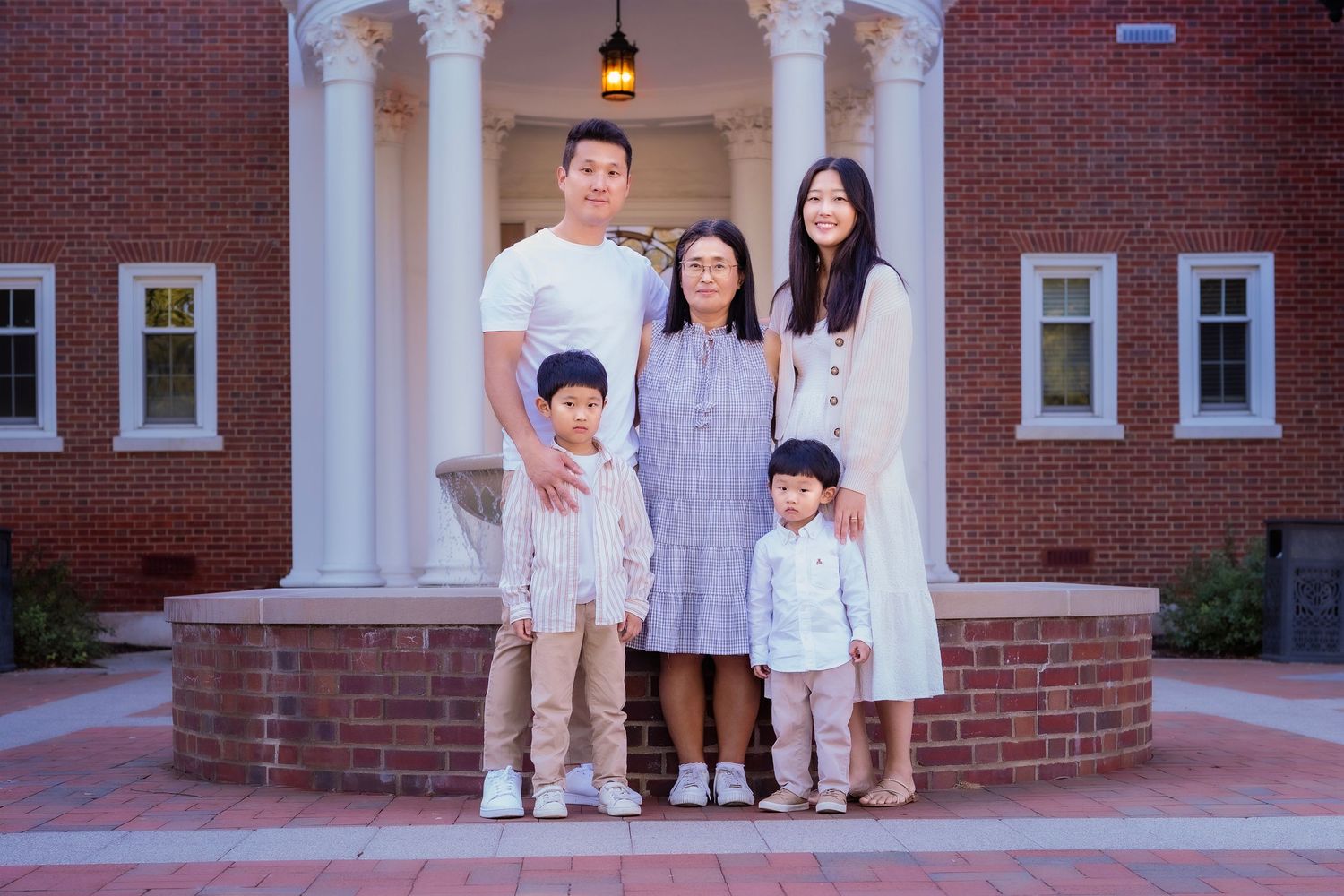 Family of five posing together in front of a brick building with white columns for a portrait photo.