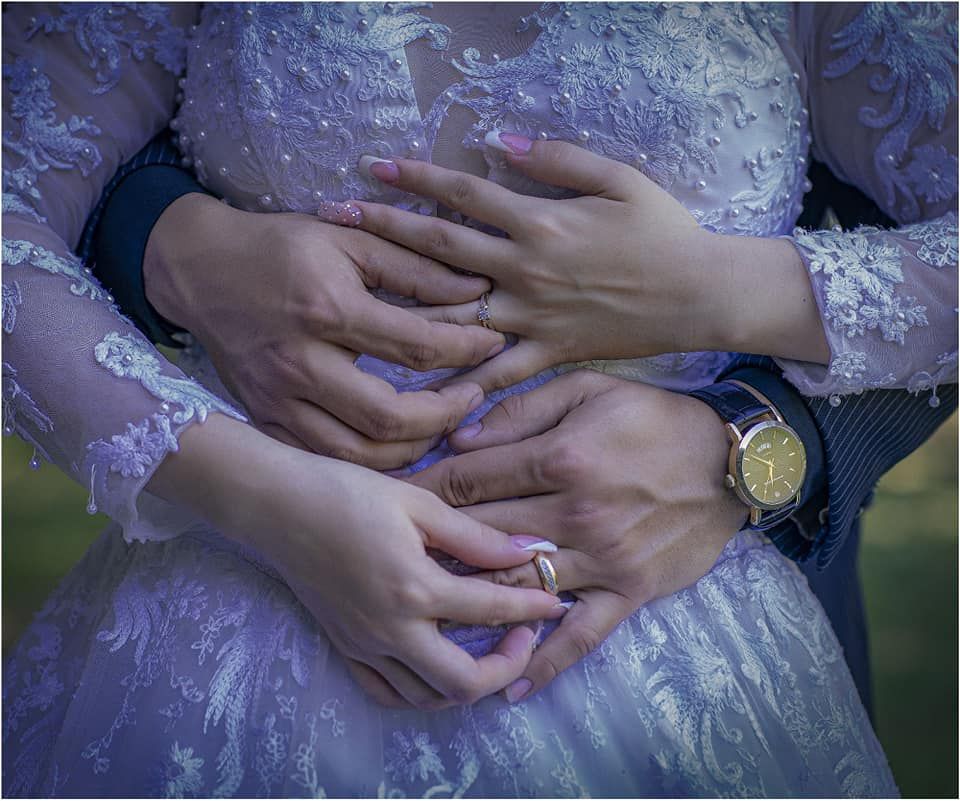 Newlywed couple holding hands, bride in lace wedding dress with diamond ring, groom wearing gold watch.
