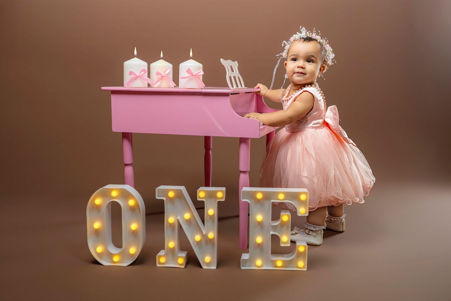 A collection of photos showing a pink tutu dress and illuminated marquee letters spelling out 'ONE' for a first birthday.