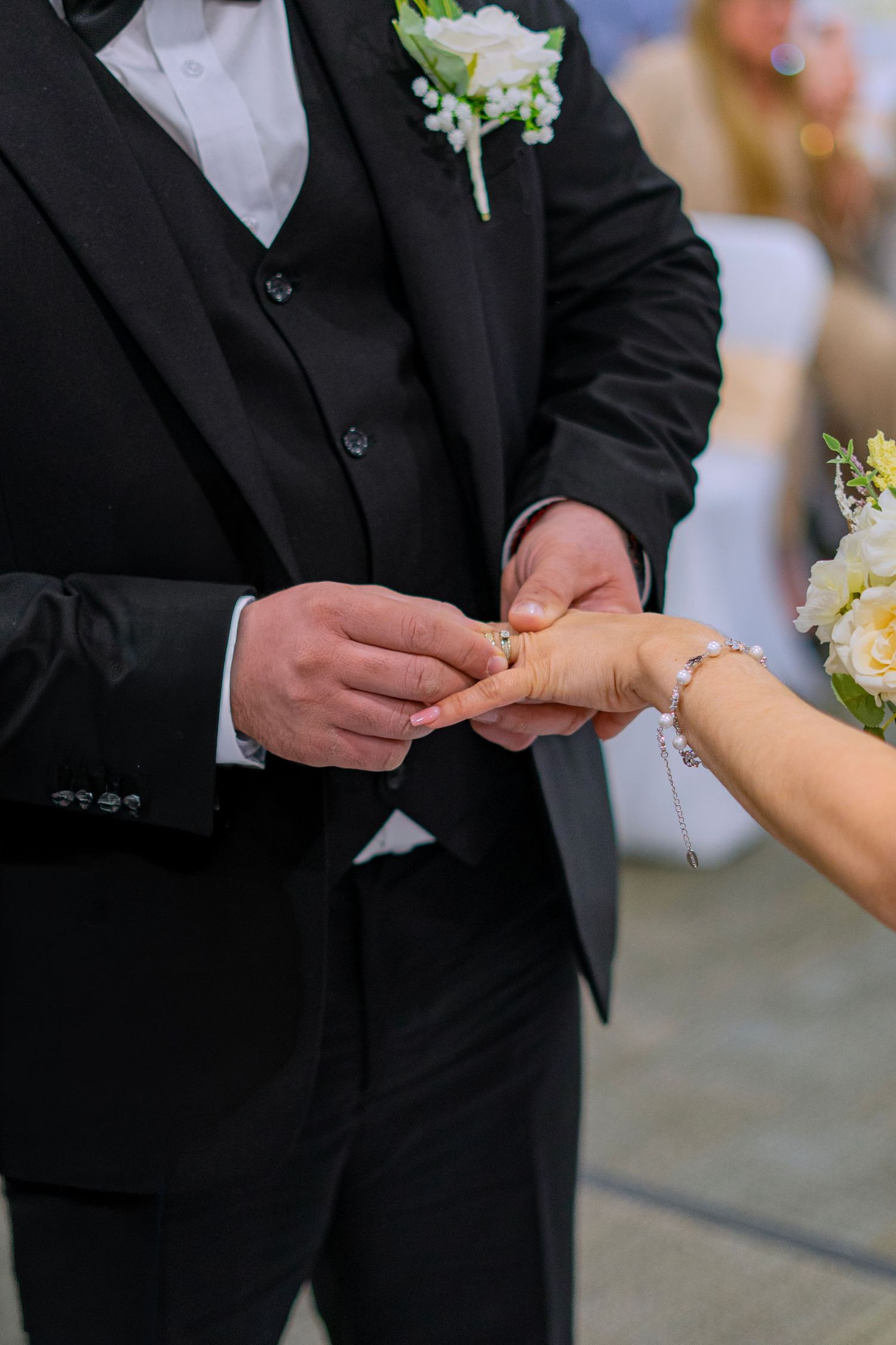 Groom in black suit placing wedding ring on bride's finger during ceremony.