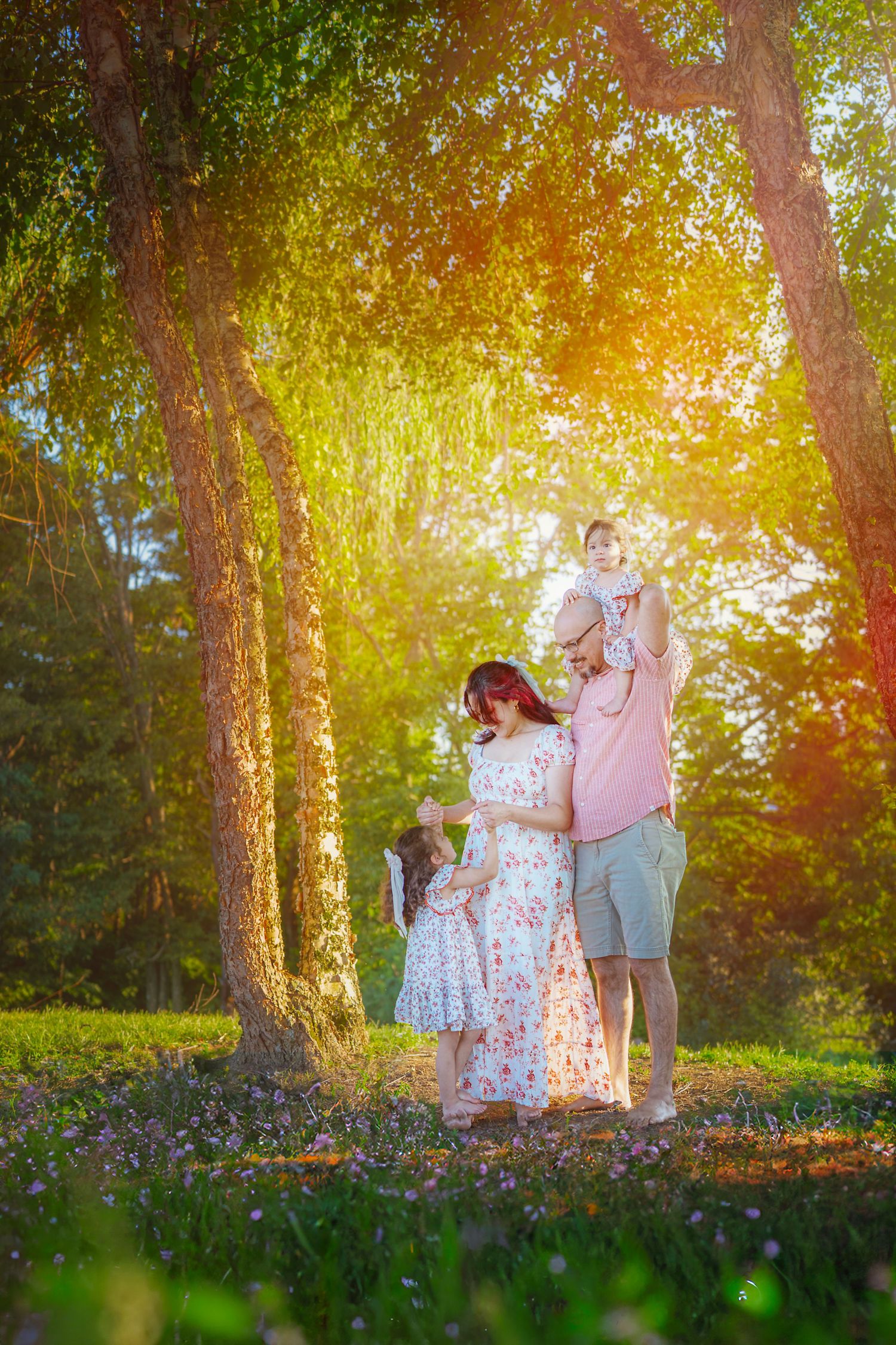 Family enjoying a sunny day in a lush green park, with a child on dad's shoulders and flowers blooming.