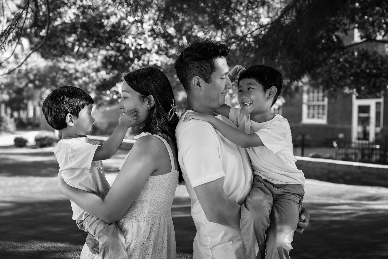 A tender black and white portrait of a family embracing outdoors on a tree-lined residential street.