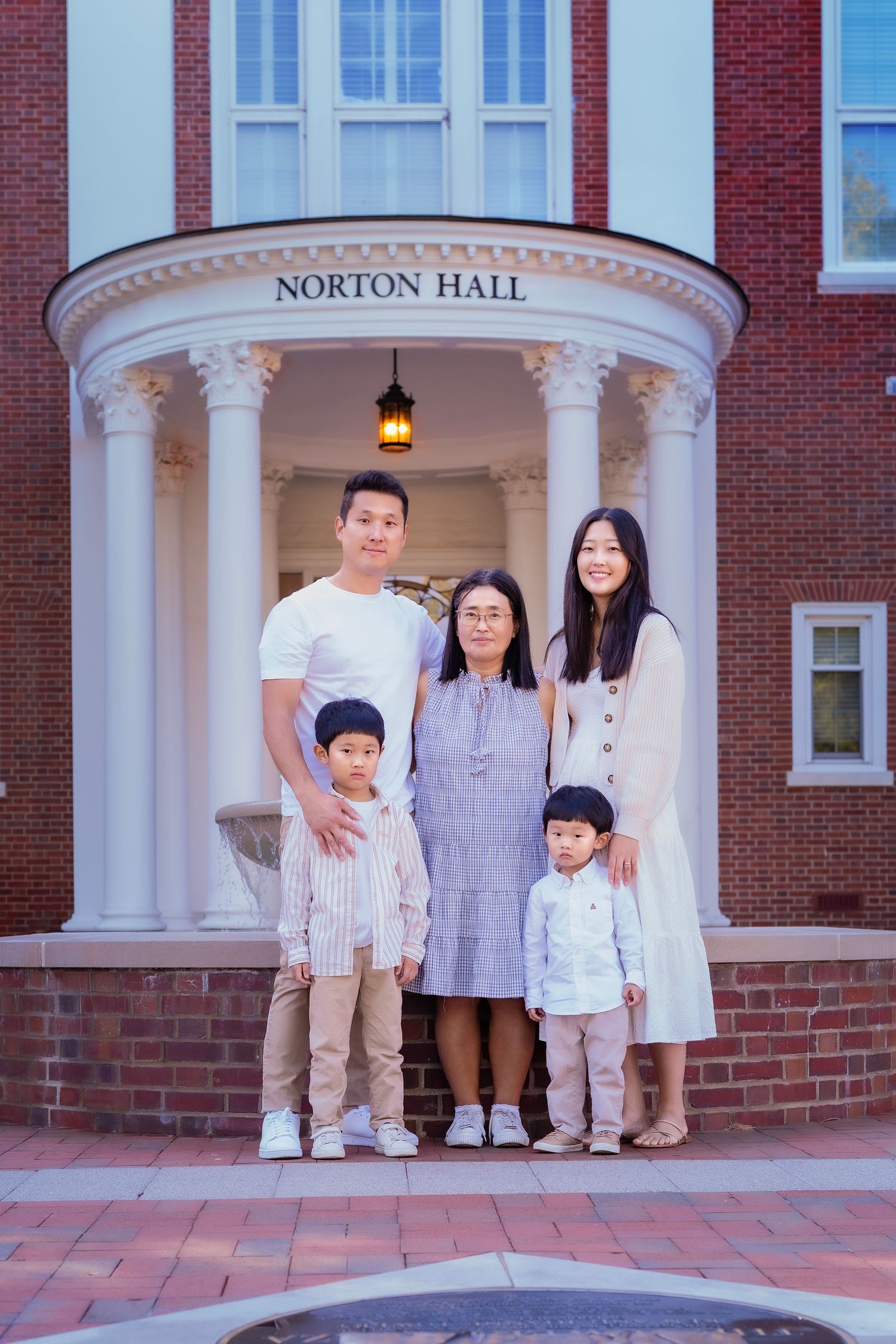 Family of five posing in front of Norton Hall brick building with white columns.
