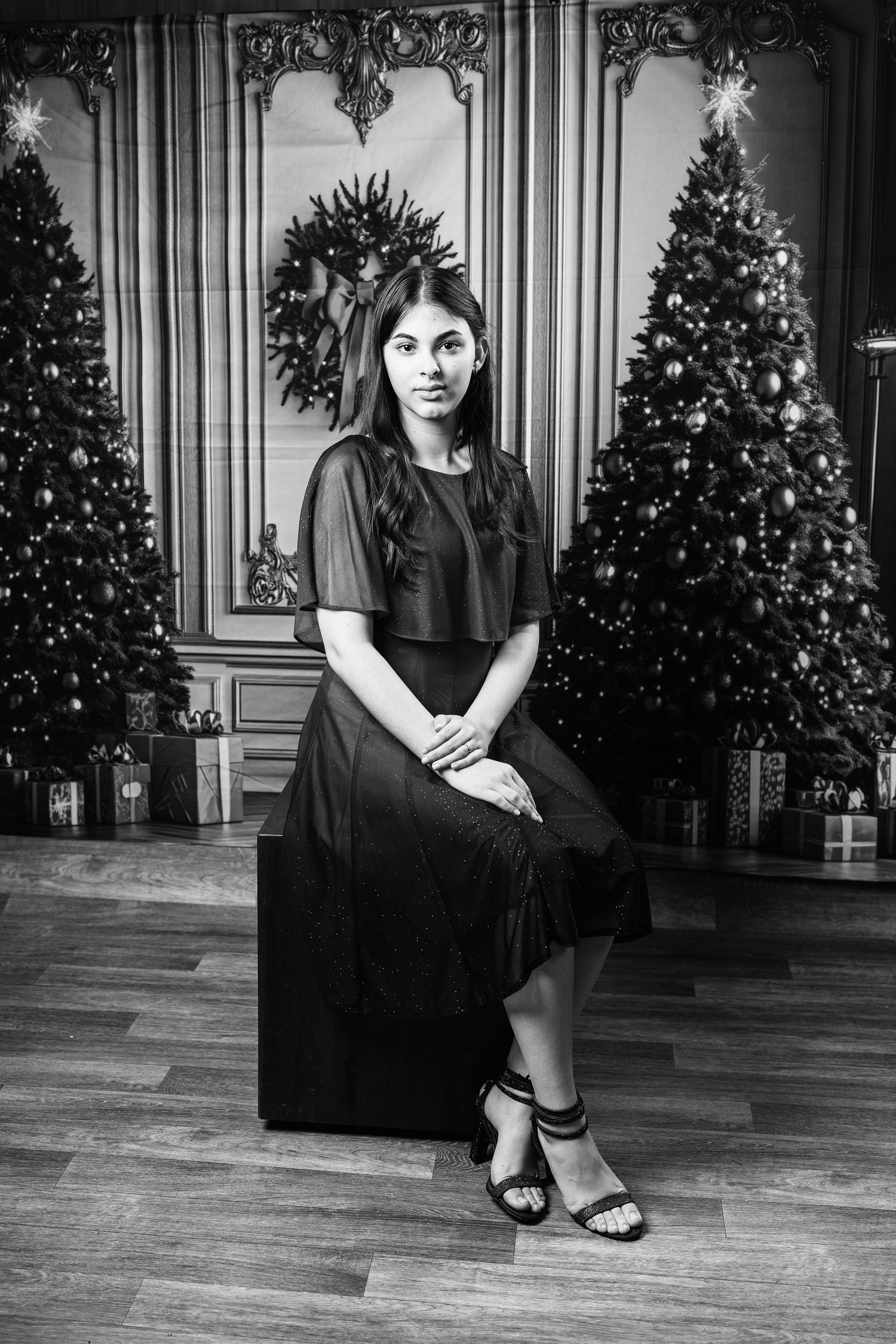 Black and white portrait series showing a woman in dark dress seated near decorated Christmas trees in an elegant room.