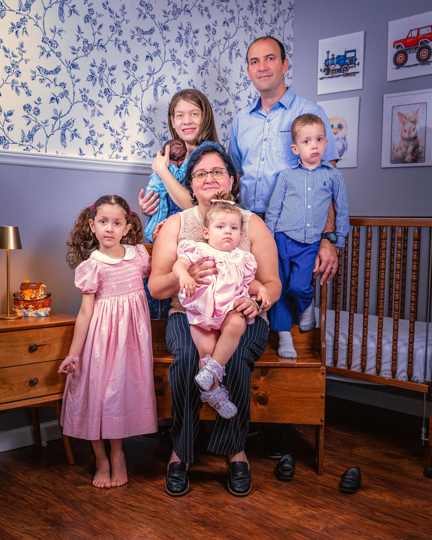 Family portrait in a nursery room with floral wallpaper, wooden furniture, and children in formal attire.