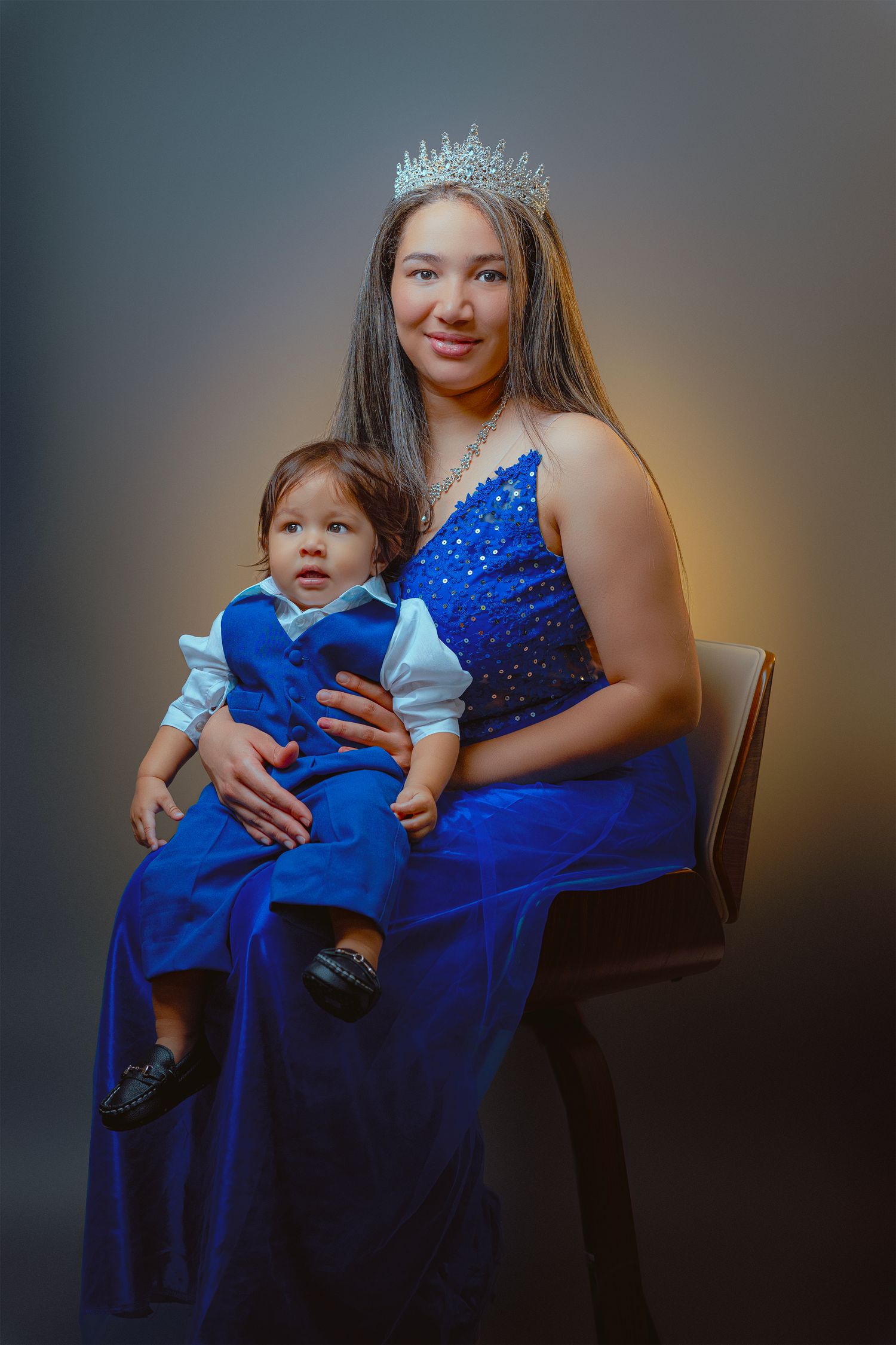 A formal portrait in blue featuring a sparkling evening gown and tiara against a dark background.