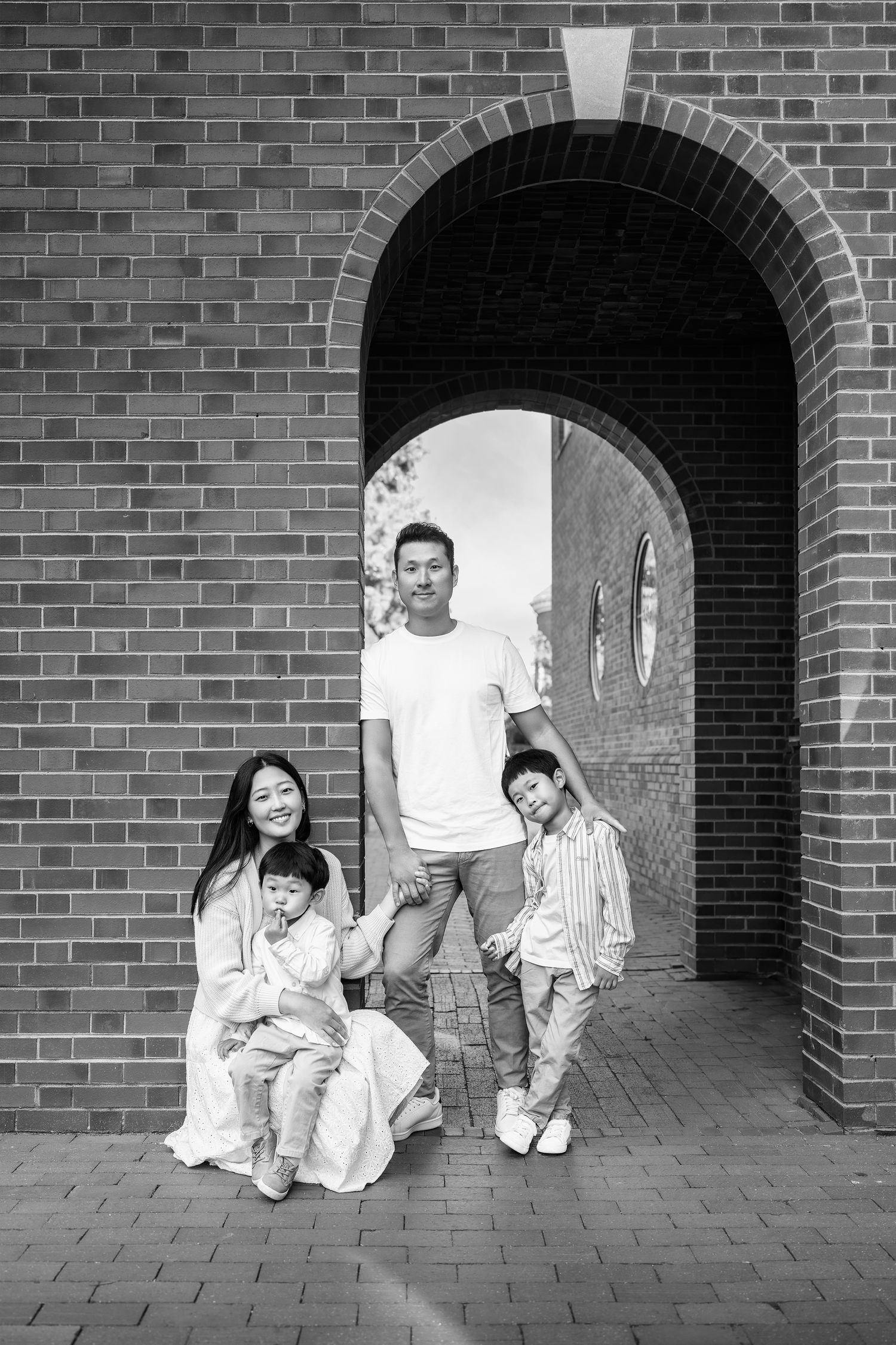A creative black and white photo sequence showing people playfully emerging from a brick archway tunnel.