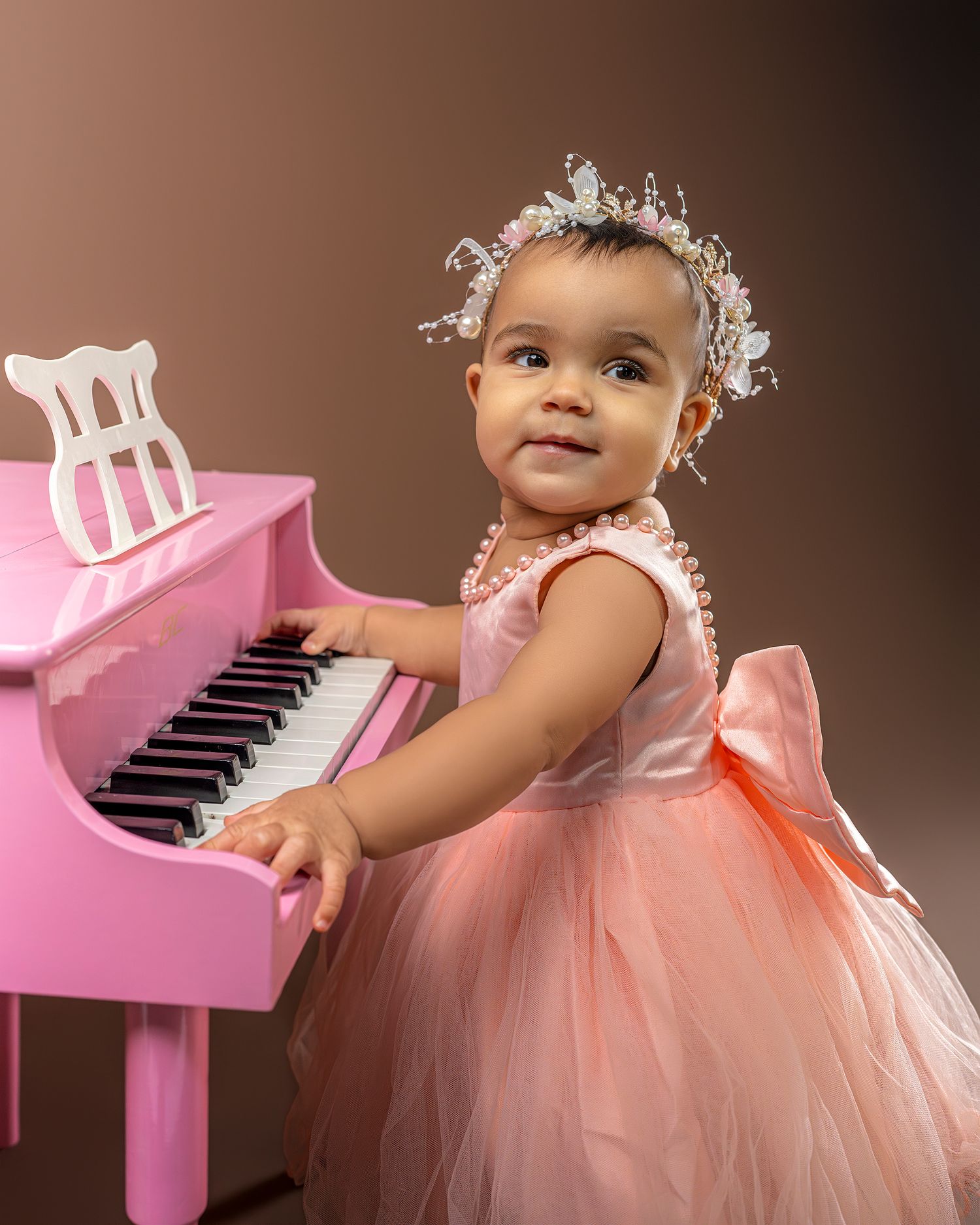 A pink toy piano with a small figure in a peach tulle dress shown in multiple artistic poses against dark background.