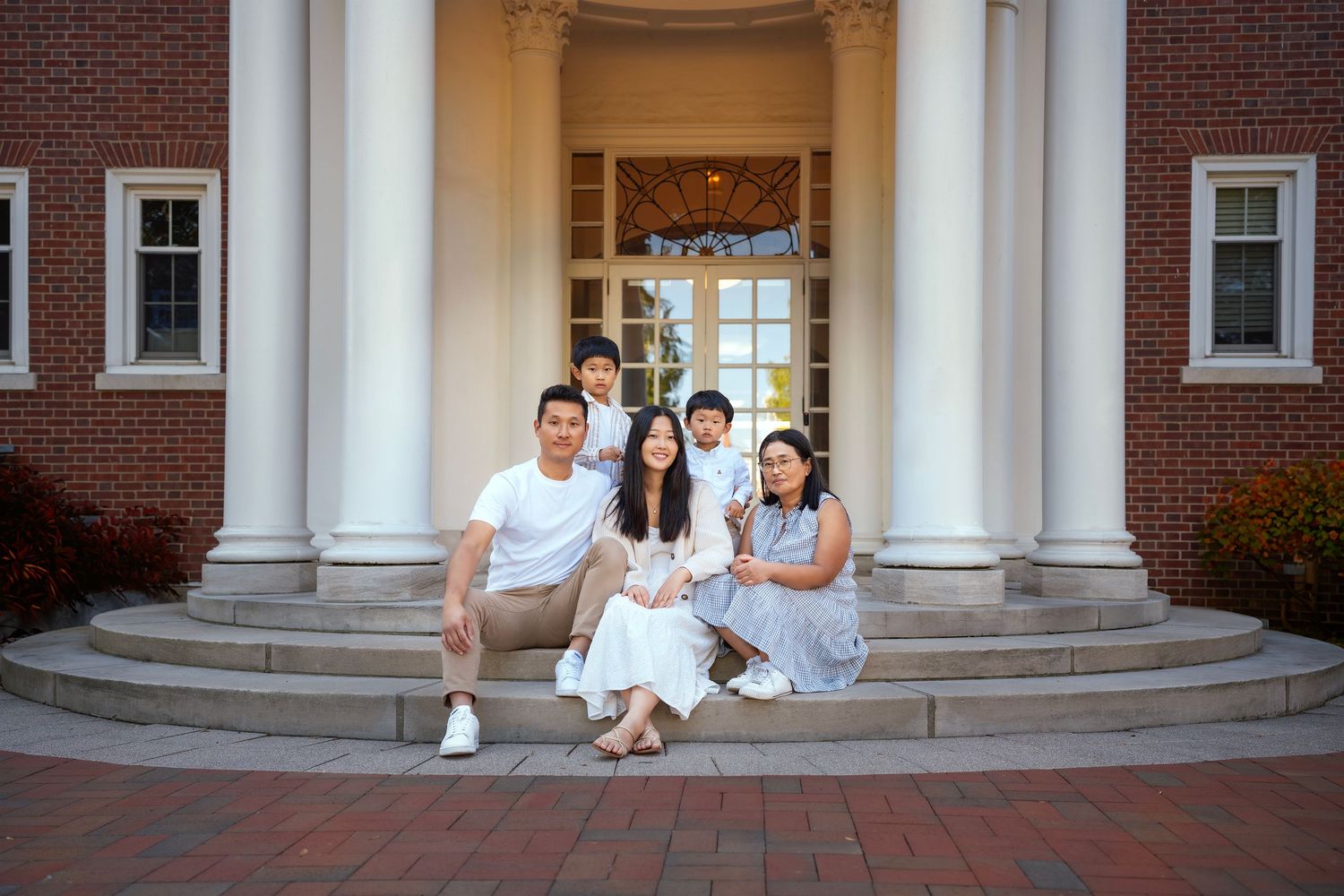Family of five posing on brick building steps, wearing white and blue outfits, smiling together outdoors.