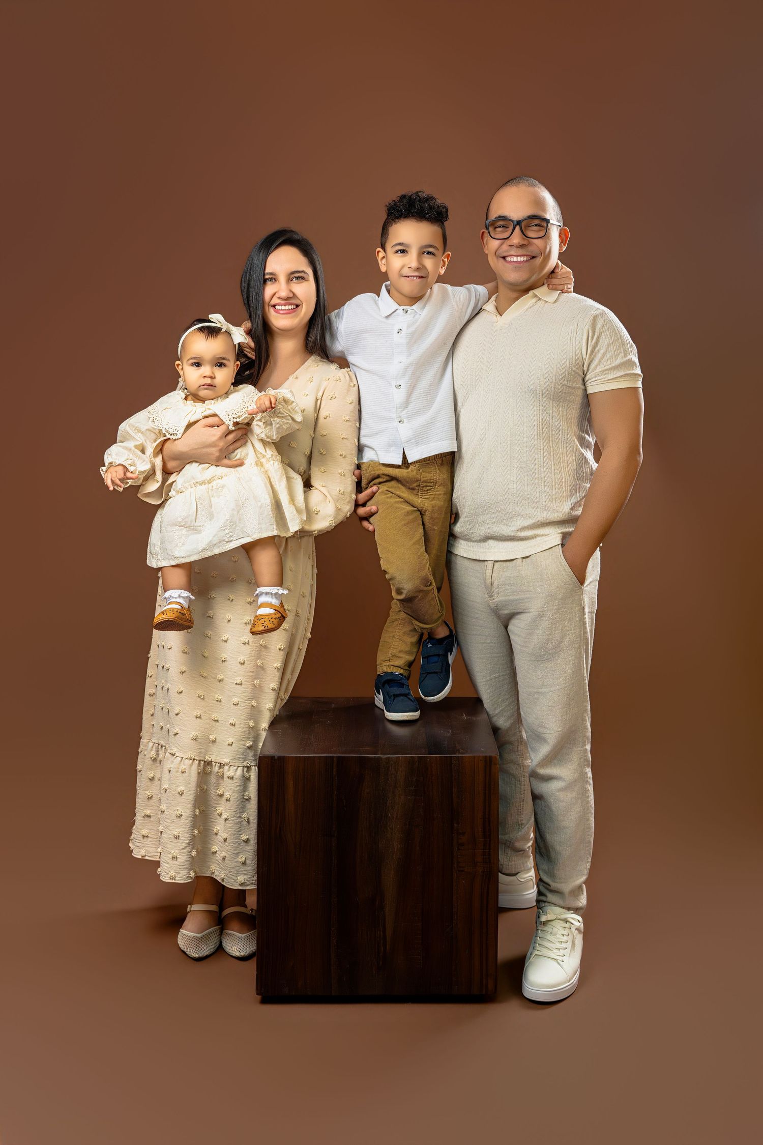 A family portrait series on brown backdrop showing progression of poses in matching cream and white outfits.