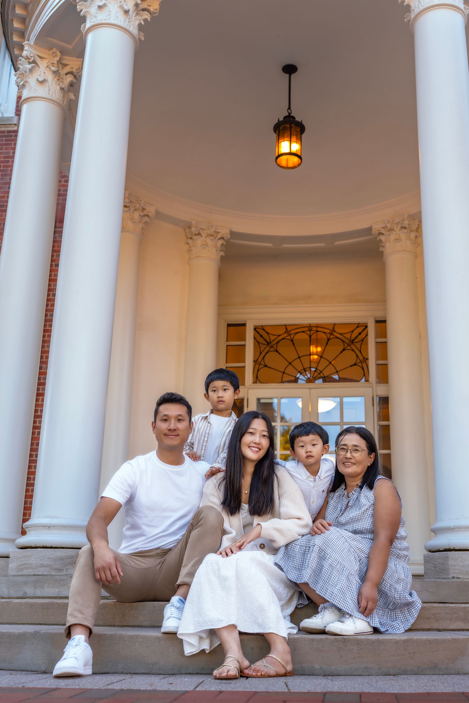 Asian family of five posing on steps of elegant building with white columns and warm lantern light.