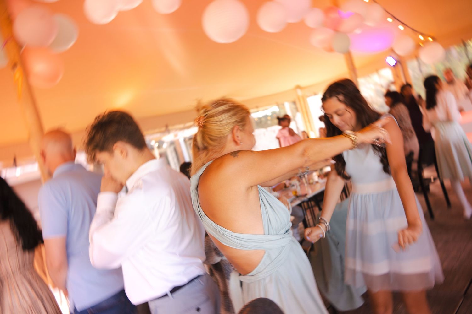 Wedding guests dance together at a reception under warm orange lighting in a banquet hall.