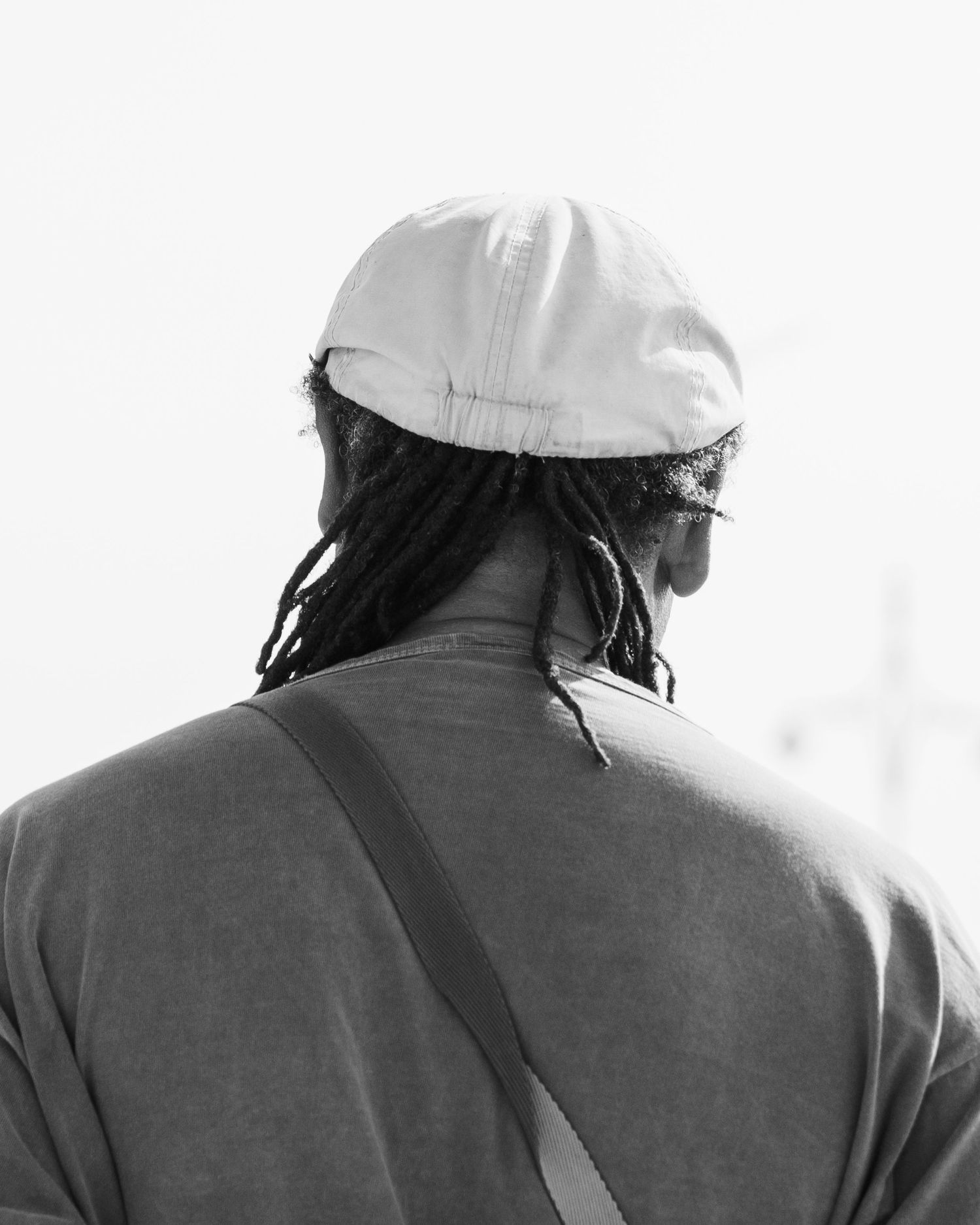 A person wearing a white cap and dark jacket is shown from behind in black and white photography.