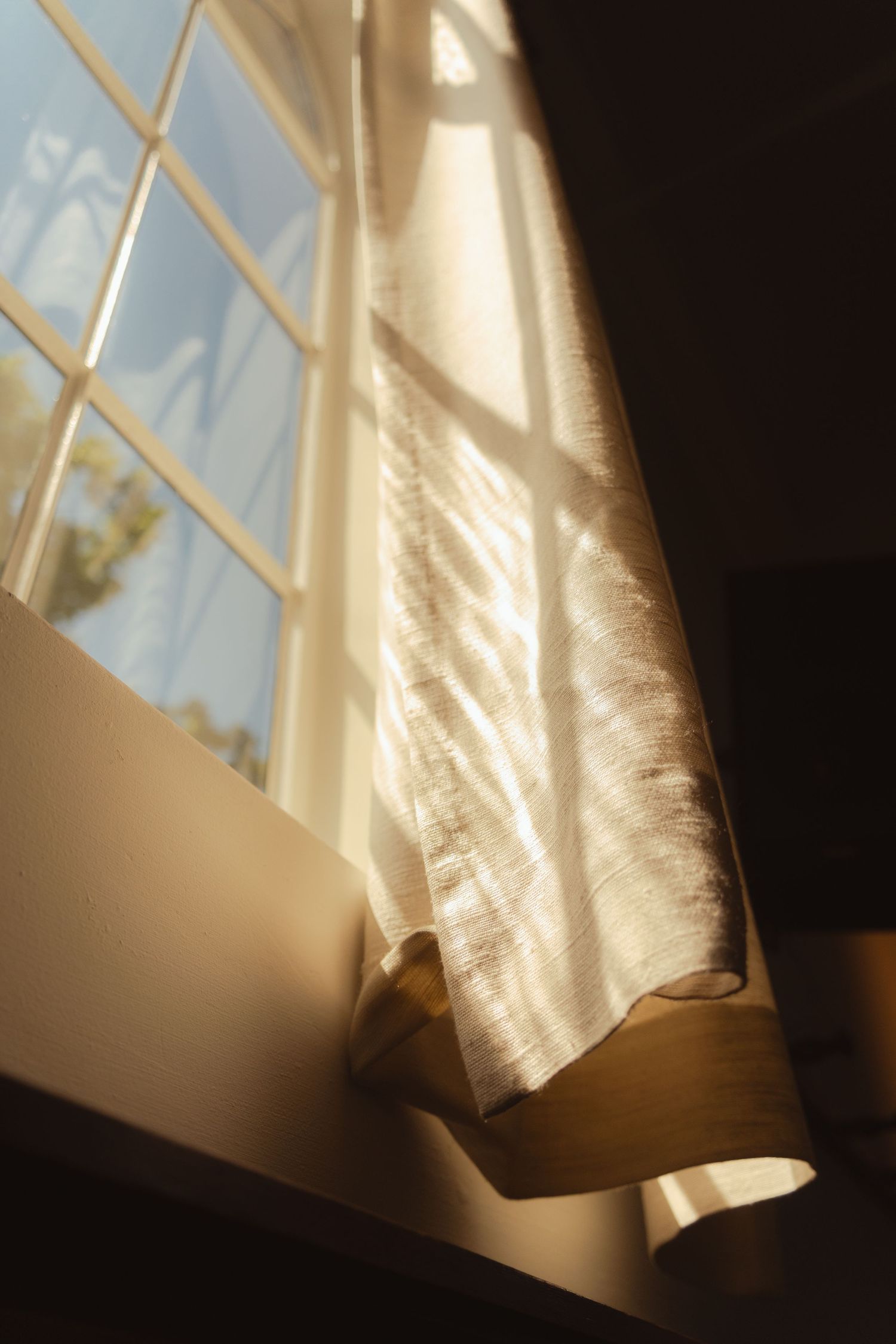 Sunlight streams through a window with blinds, creating dramatic shadows and light patterns on a curtain.