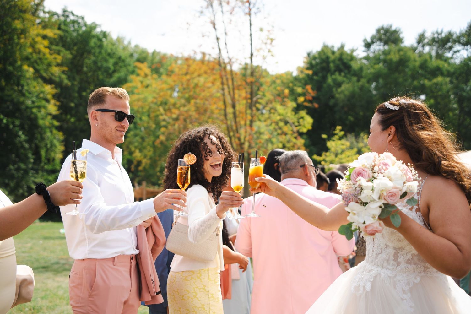 Festive wedding party celebrates with champagne toasts outdoors on a sunny autumn day.
