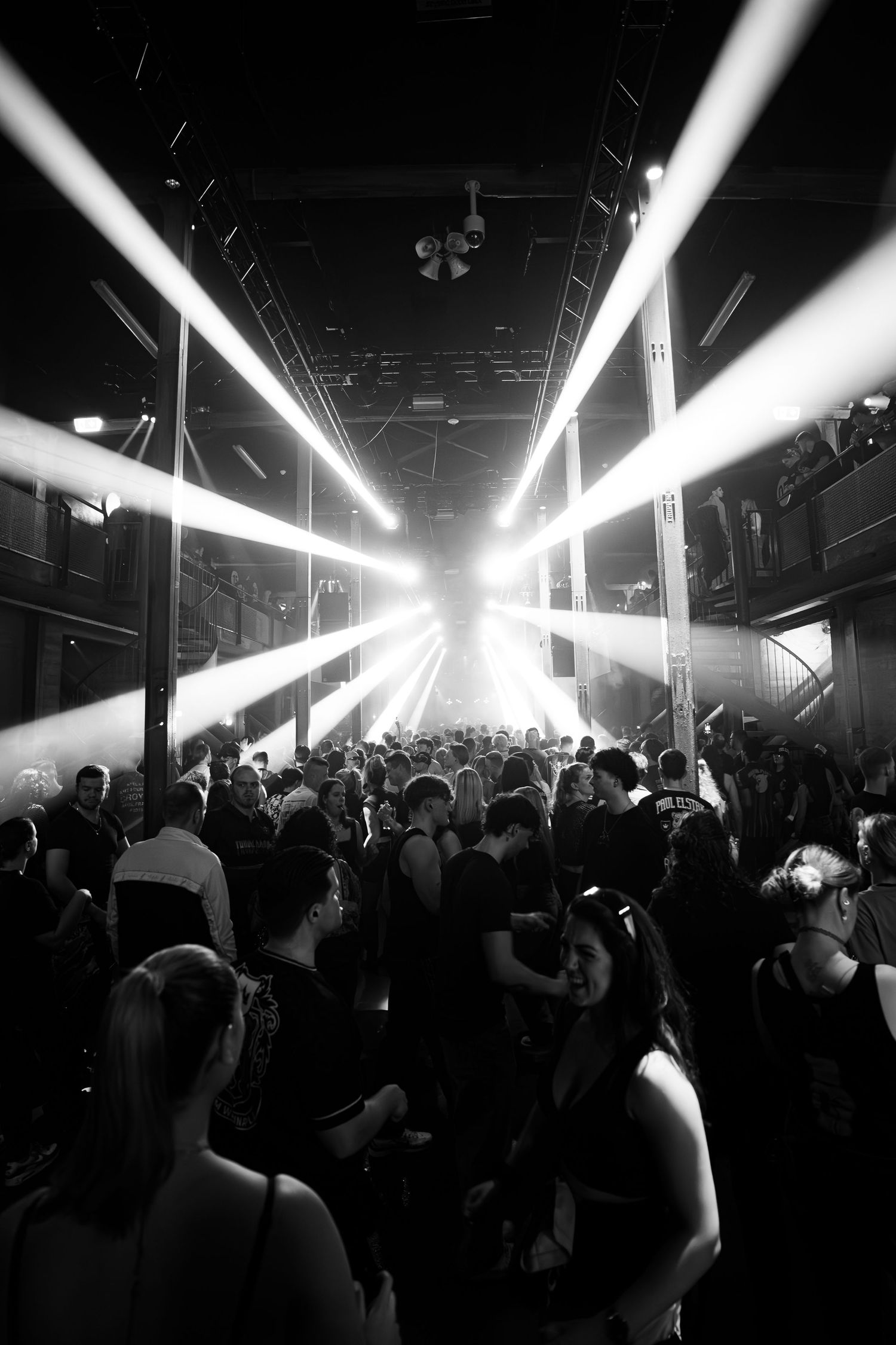 Silhouetted crowd dances in a nightclub under dramatic white strobe lights creating an energetic party atmosphere.