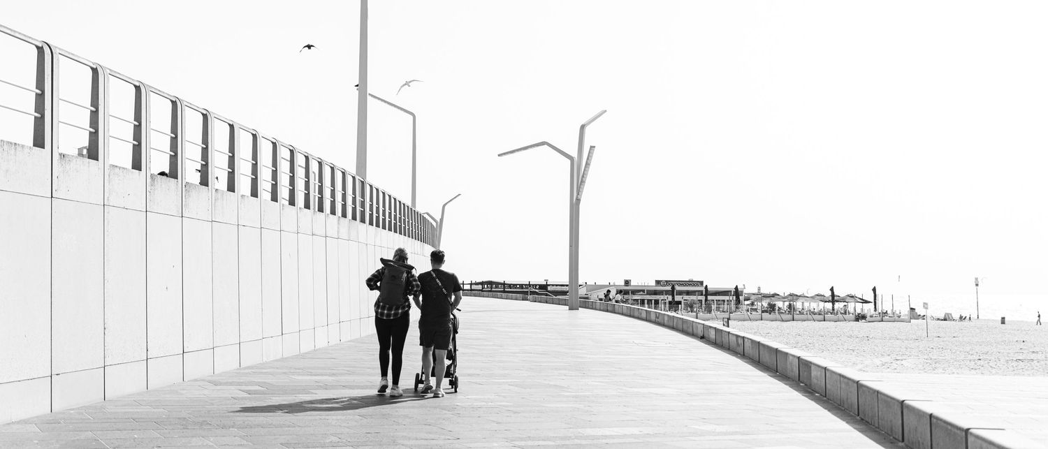 Three black figures walk across a stark white slope in a minimalist architectural setting with converging lines.