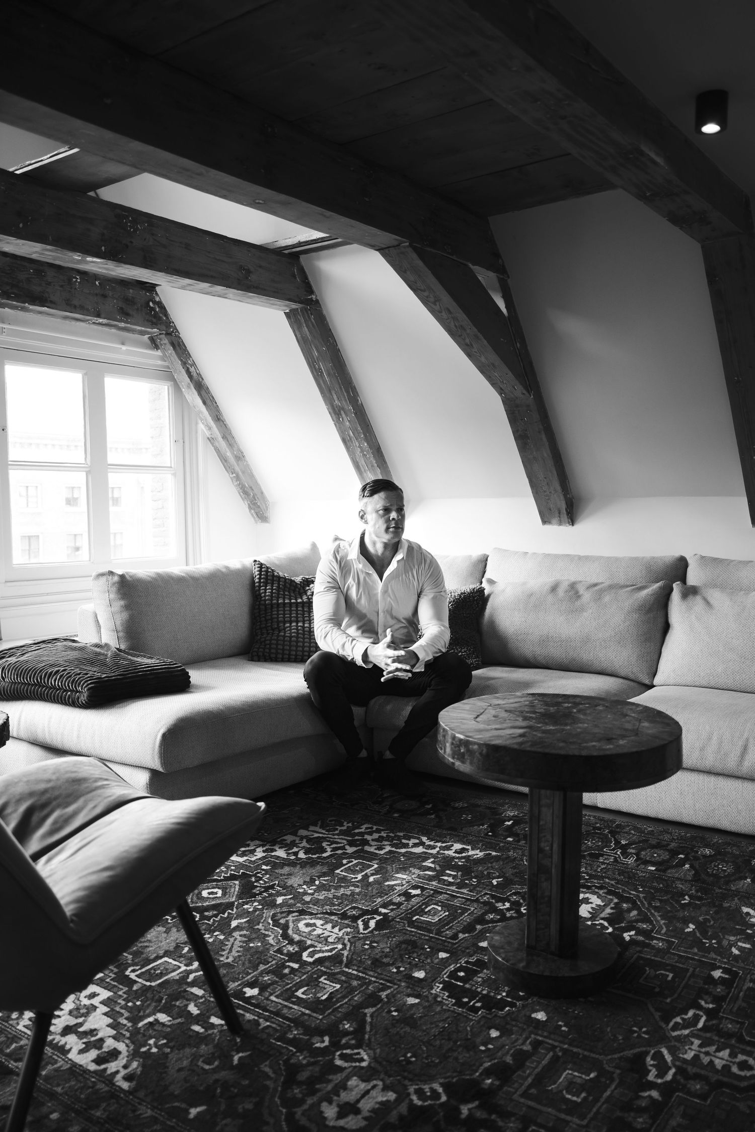 Black and white photo series showing a minimalist attic room with white couch and patterned rug in different angles.