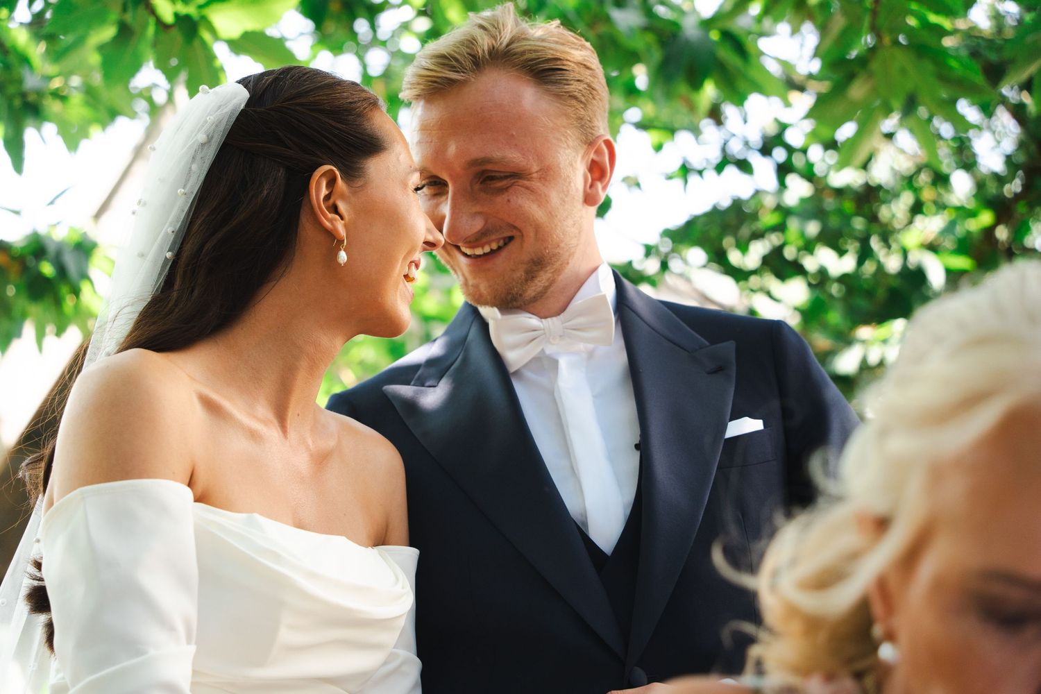 A romantic outdoor wedding ceremony scene with lush green foliage overhead creating a natural canopy.