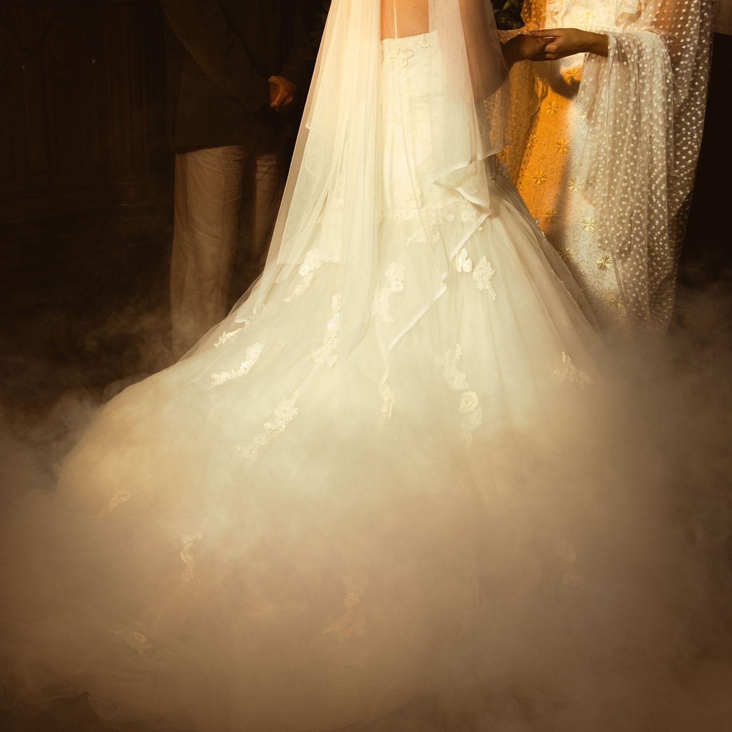 White wedding dress with a flowing train and veil displayed in warm lighting creating a romantic atmosphere.