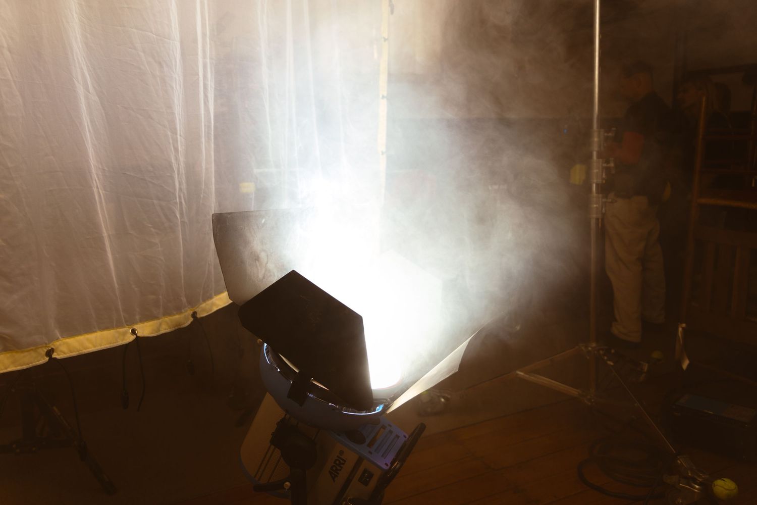 A fog machine creates atmospheric smoke effects in a dimly lit room, casting dramatic beams of light.