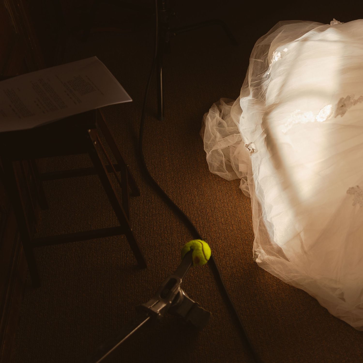 Tennis ball and clamp light illuminate white fabric against dark background in moody studio setup.