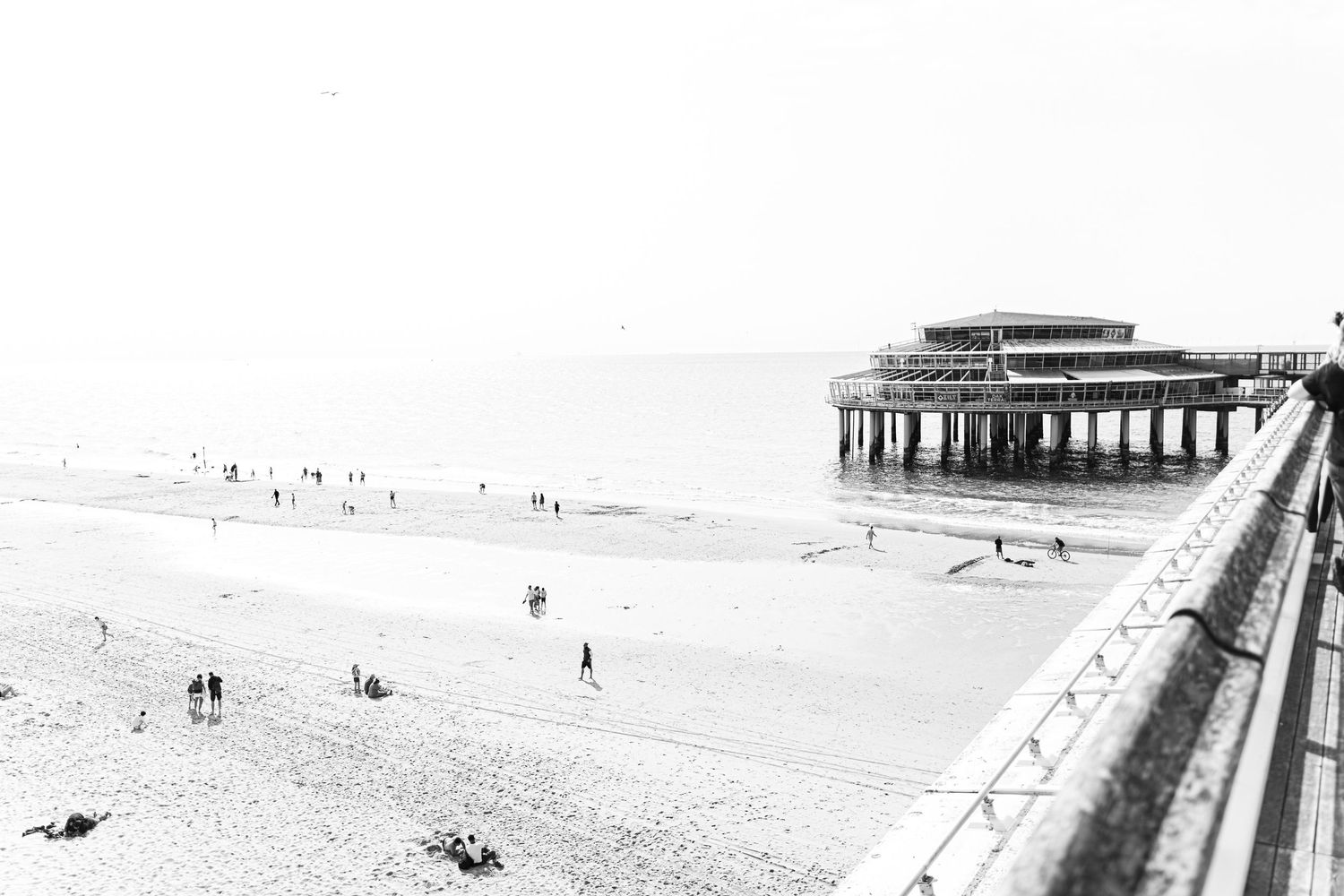 A scenic view of a long pier extending into the ocean with beachgoers visible in the distance.