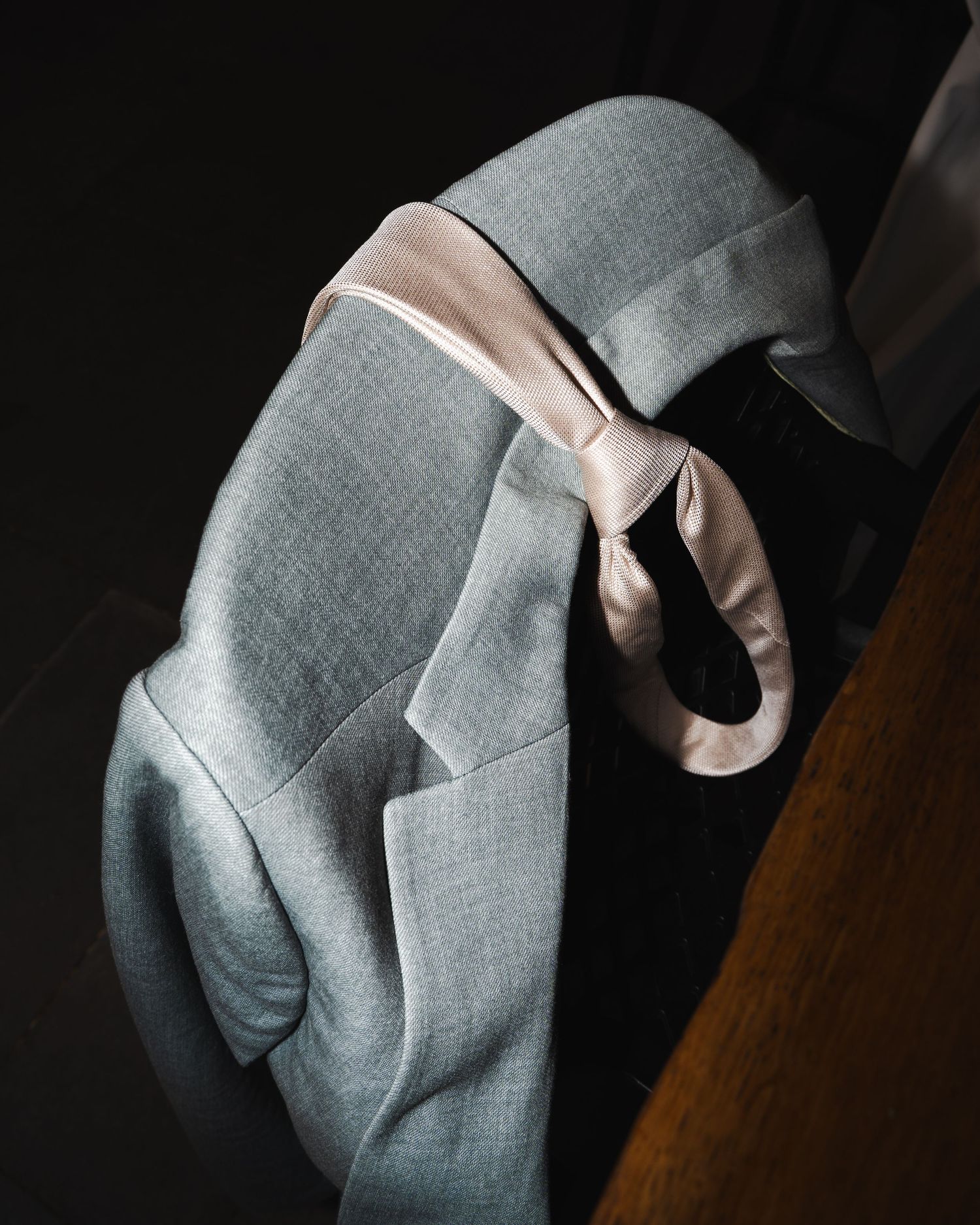 Close-up details of a light gray suit jacket with a pink bow accent against a dark background.