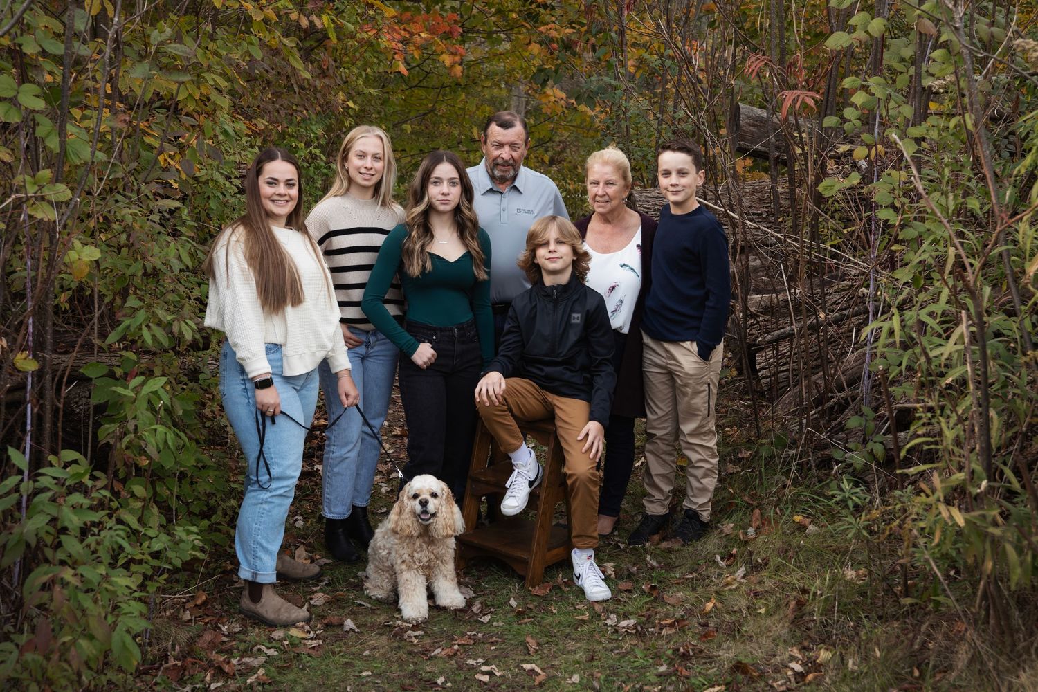 Large group sitting together outdoors for a family photo session in wooded fall setting.