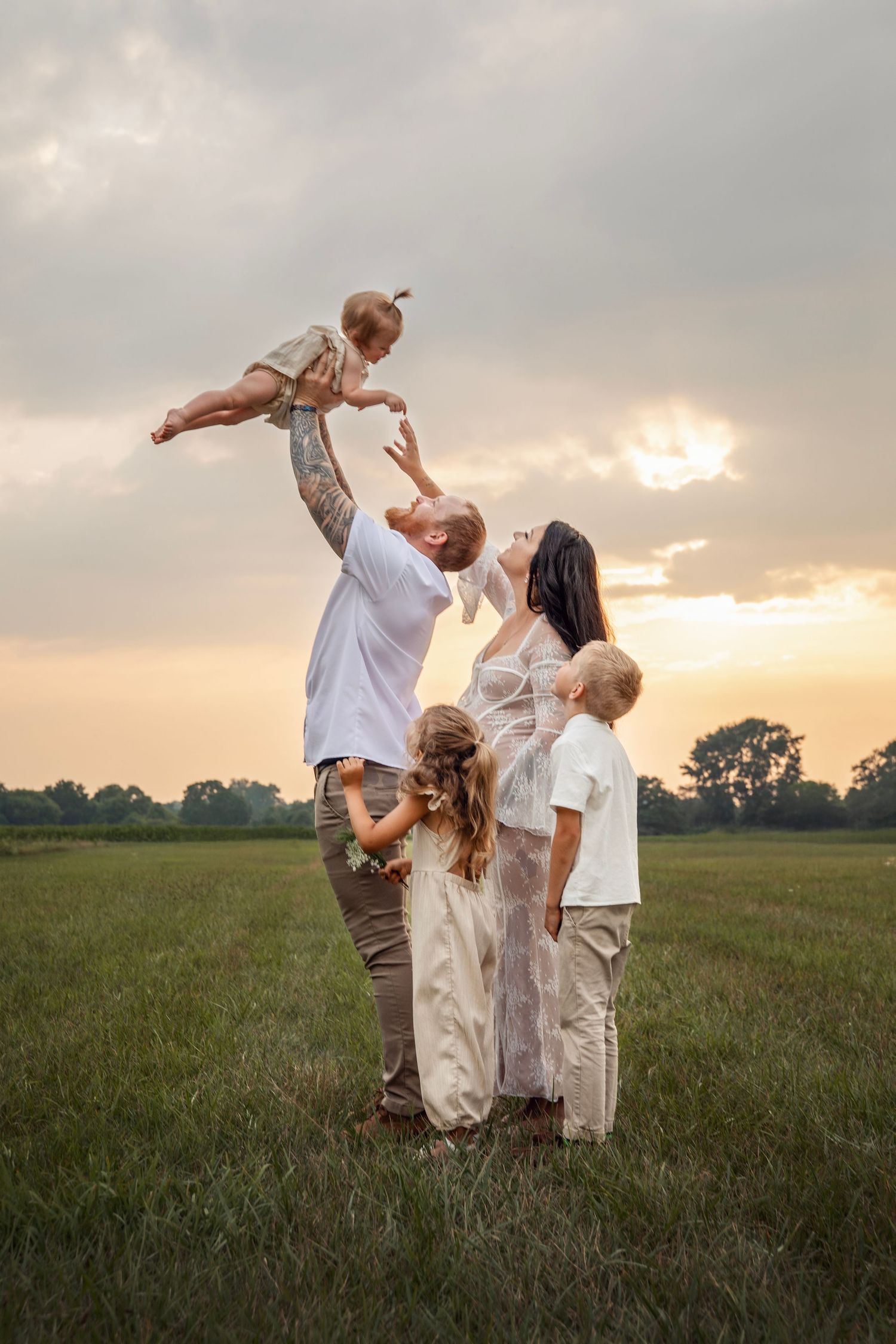 Family in coordinated white and khaki outfits playing together in a grassy field at sunset.