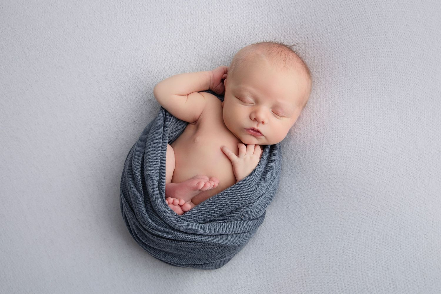 Baby sleeping peacefully while swaddled in grey fabric against light background.