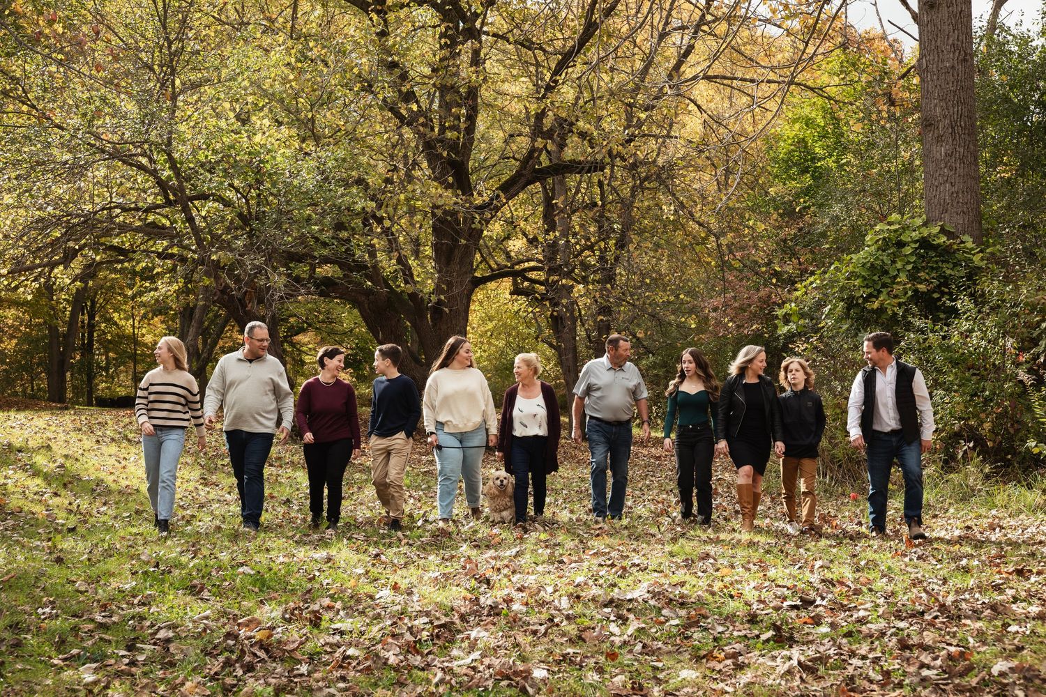 Large family group stands in line among fallen leaves for outdoor autumn portrait.
