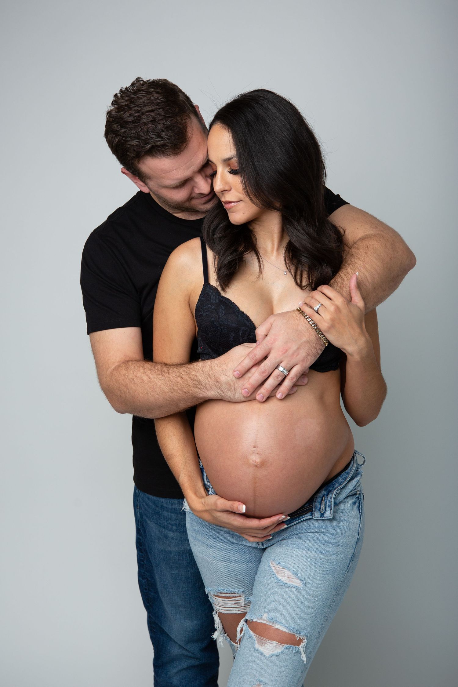 Intimate maternity portrait showing couple embracing against light backdrop.