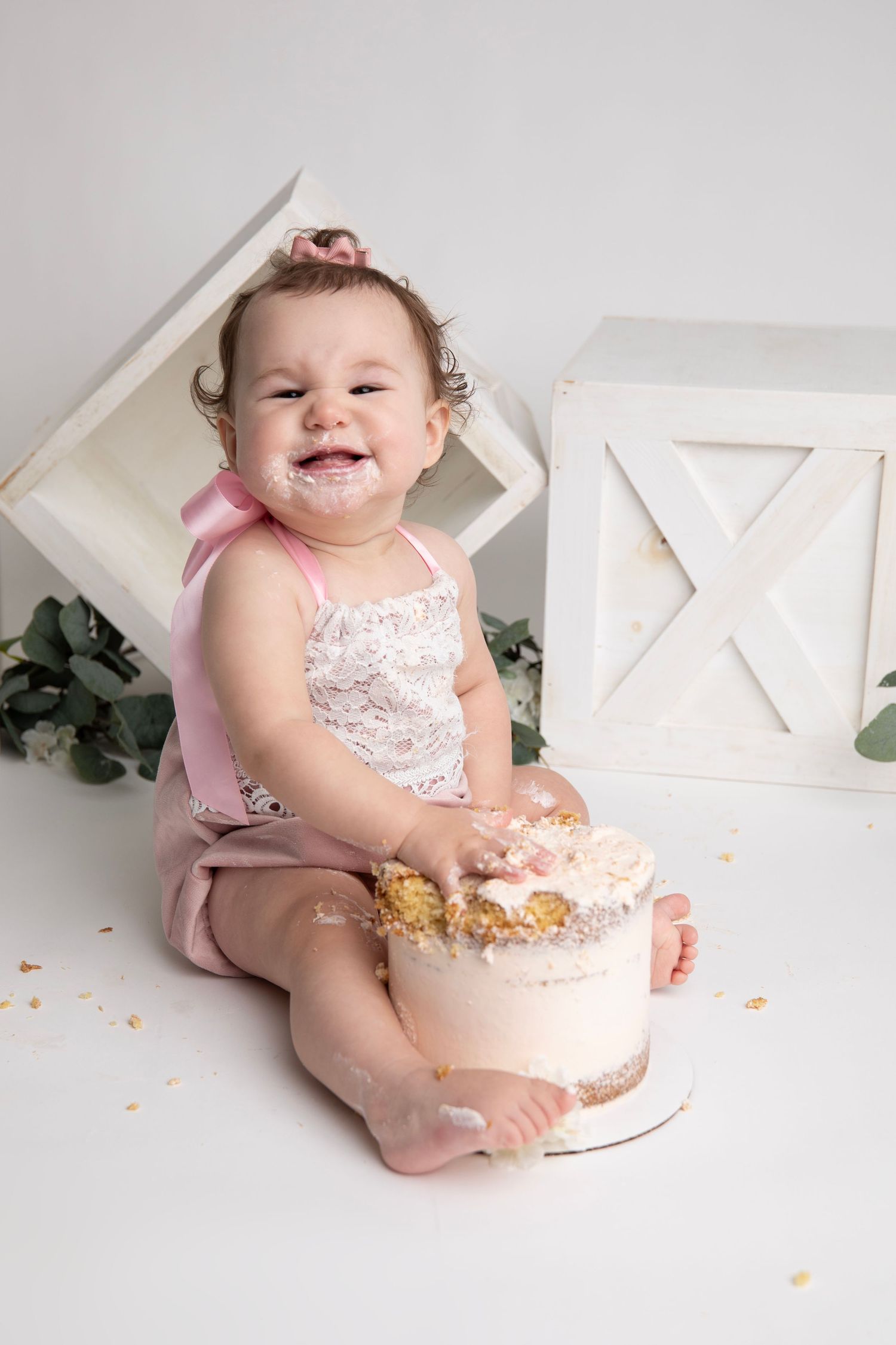 Baby in pink outfit enjoying cake smash photo session with white geometric props.