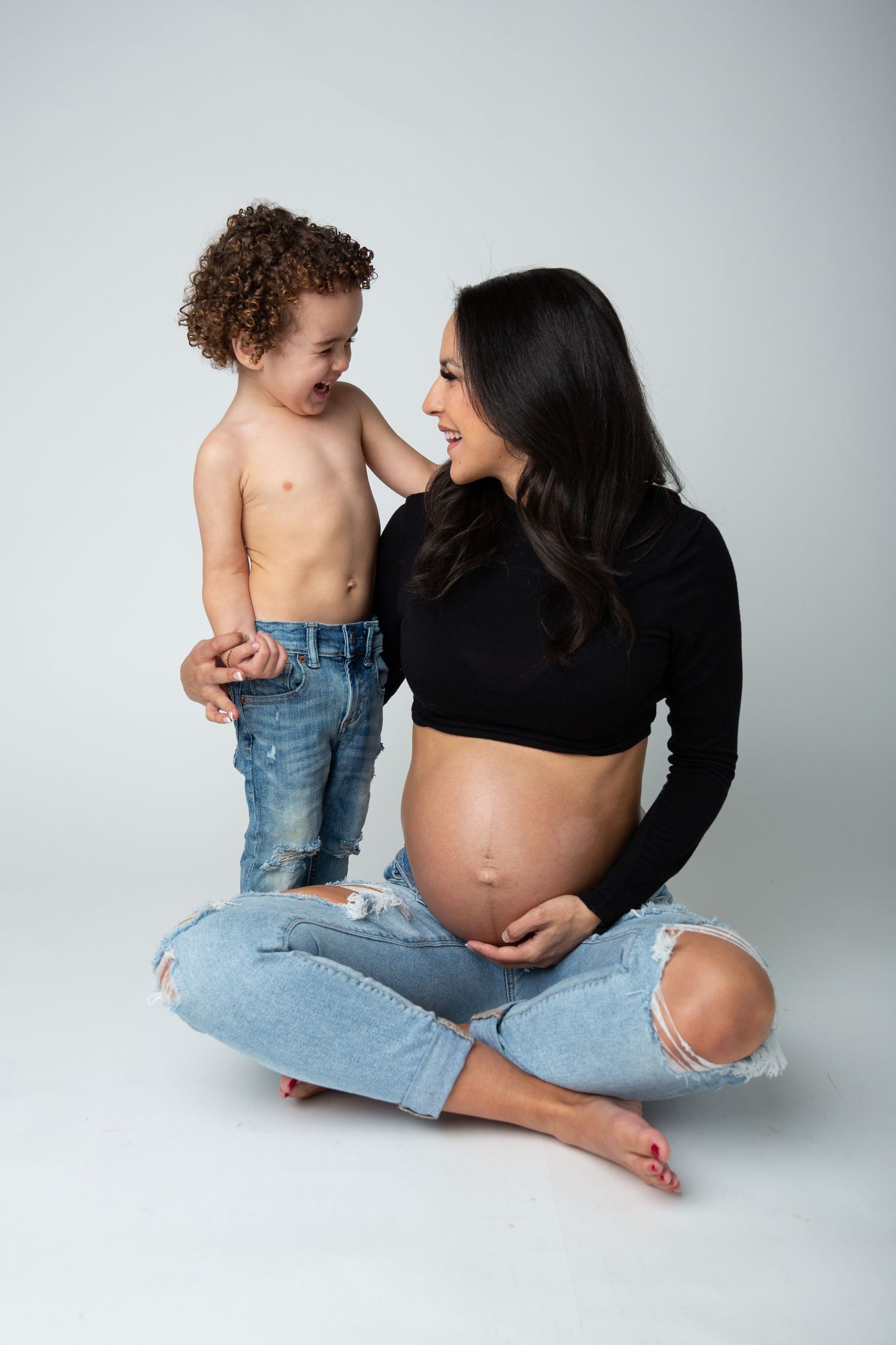 Mother and child share tender moment during maternity photoshoot on white background.