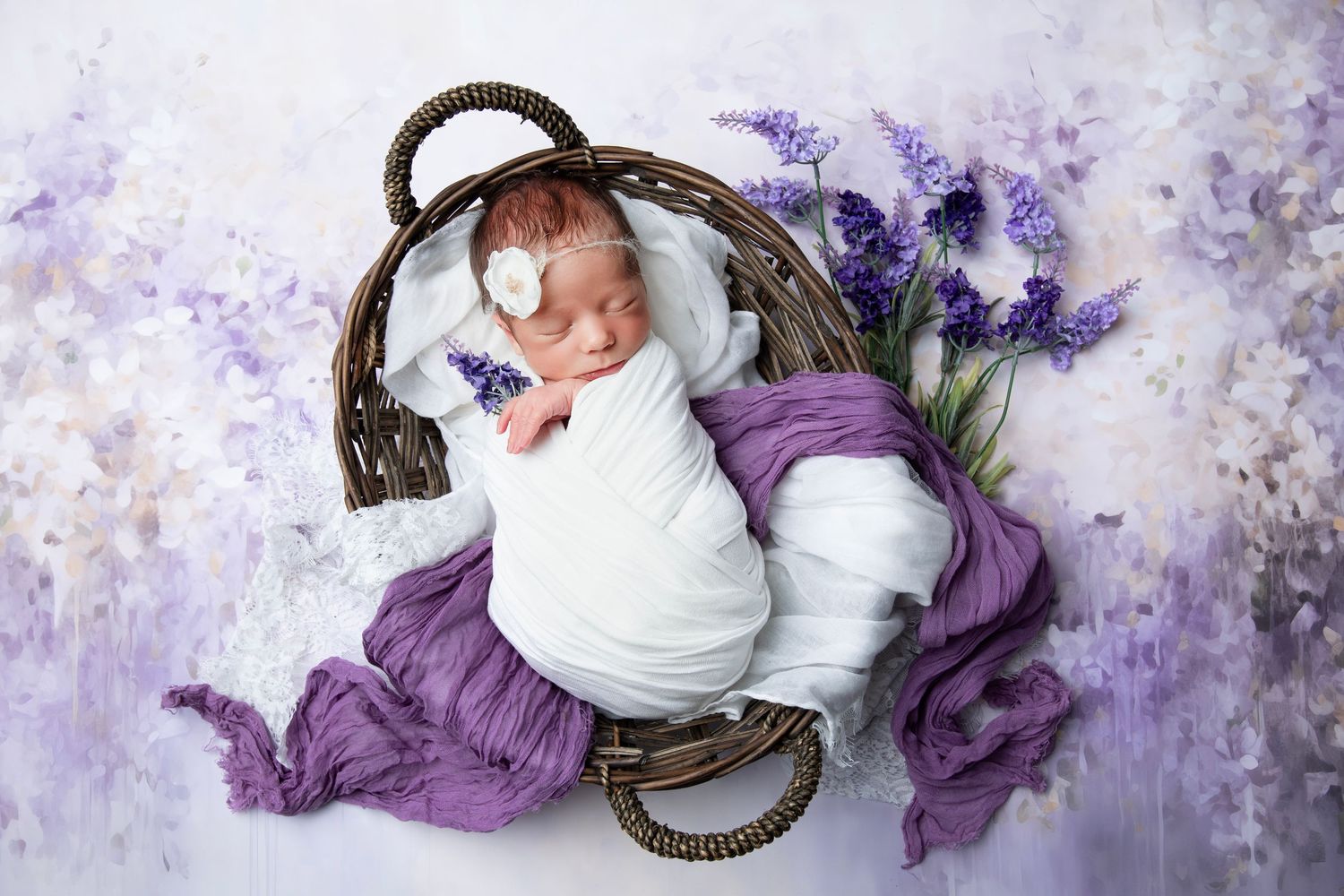 Newborn baby photographed with purple flowers and fabric in dreamy lighting setup.