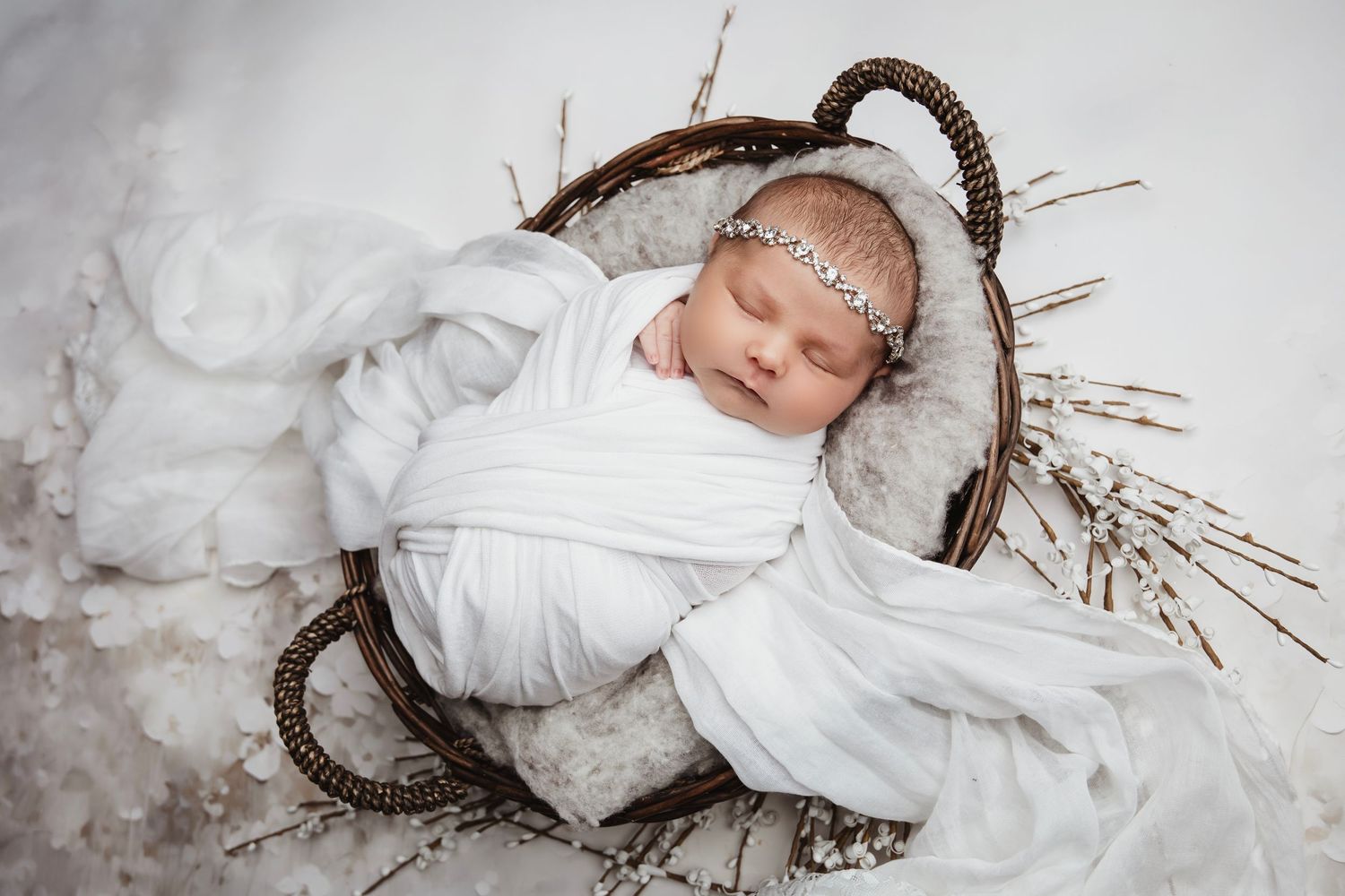 Winter themed newborn photo session with white wrapping and twigs creating halo effect.