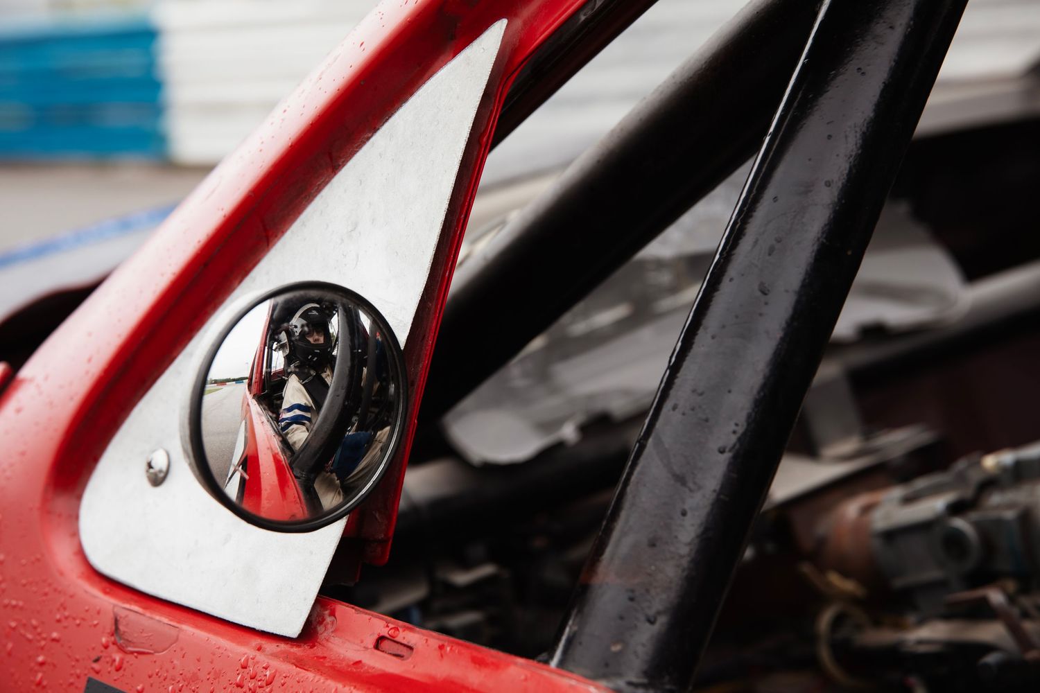 A black dog peeks through the side mirror of a red car, creating a reflective portrait.