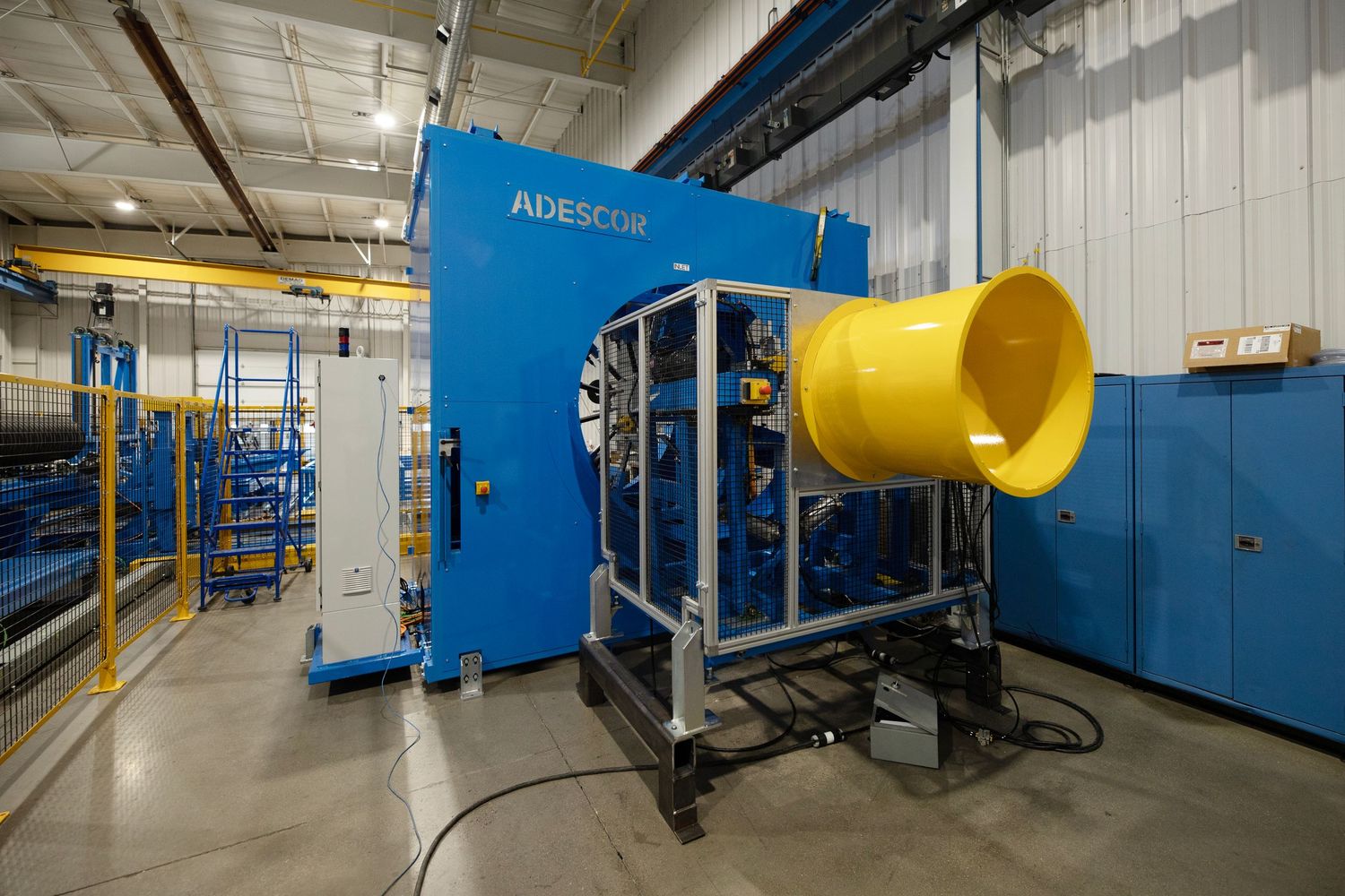 Industrial manufacturing equipment with large blue machinery and yellow cylindrical component in a factory setting.