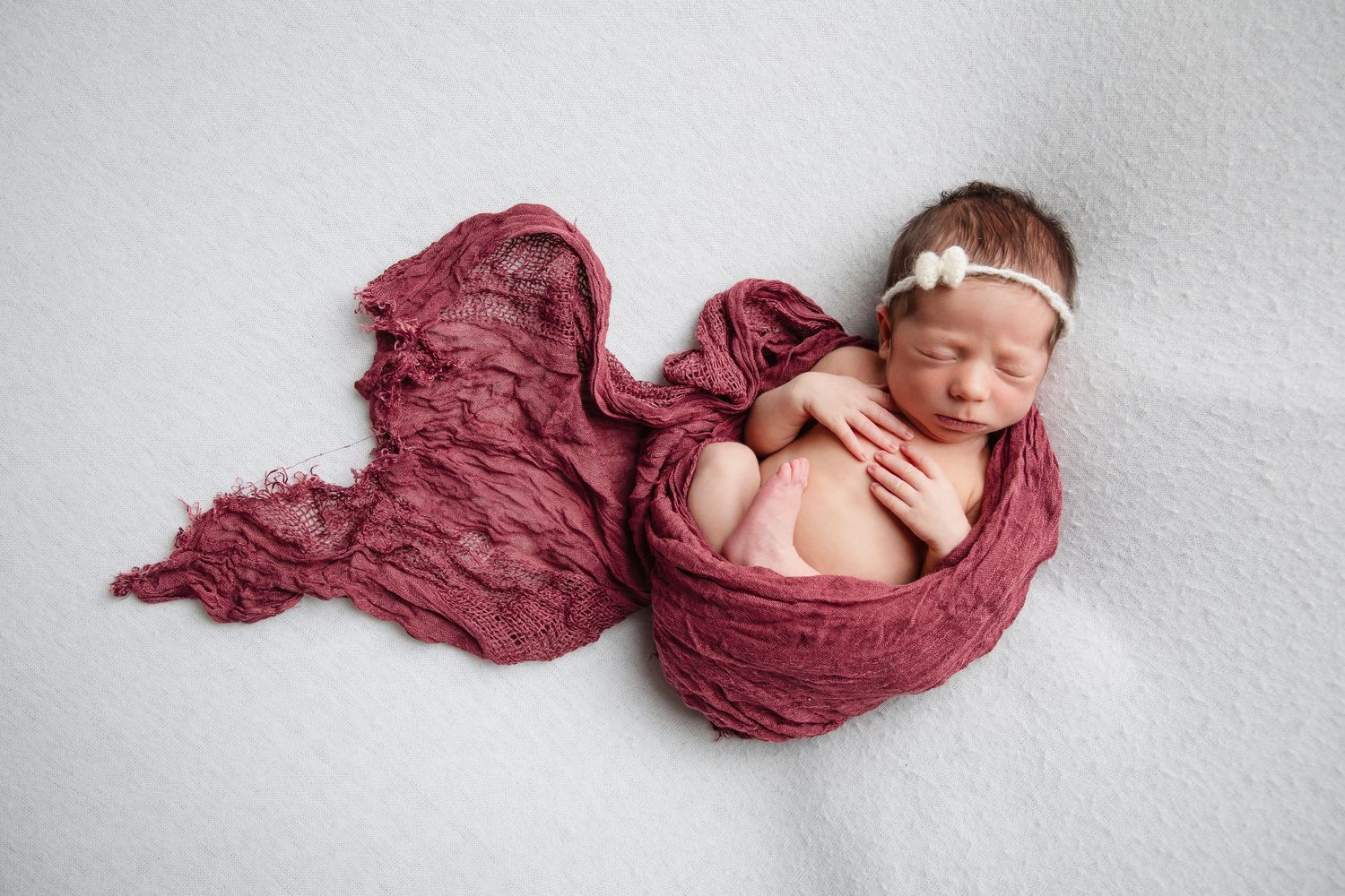 Newborn baby peacefully resting on burgundy fabric in artistic arrangement.