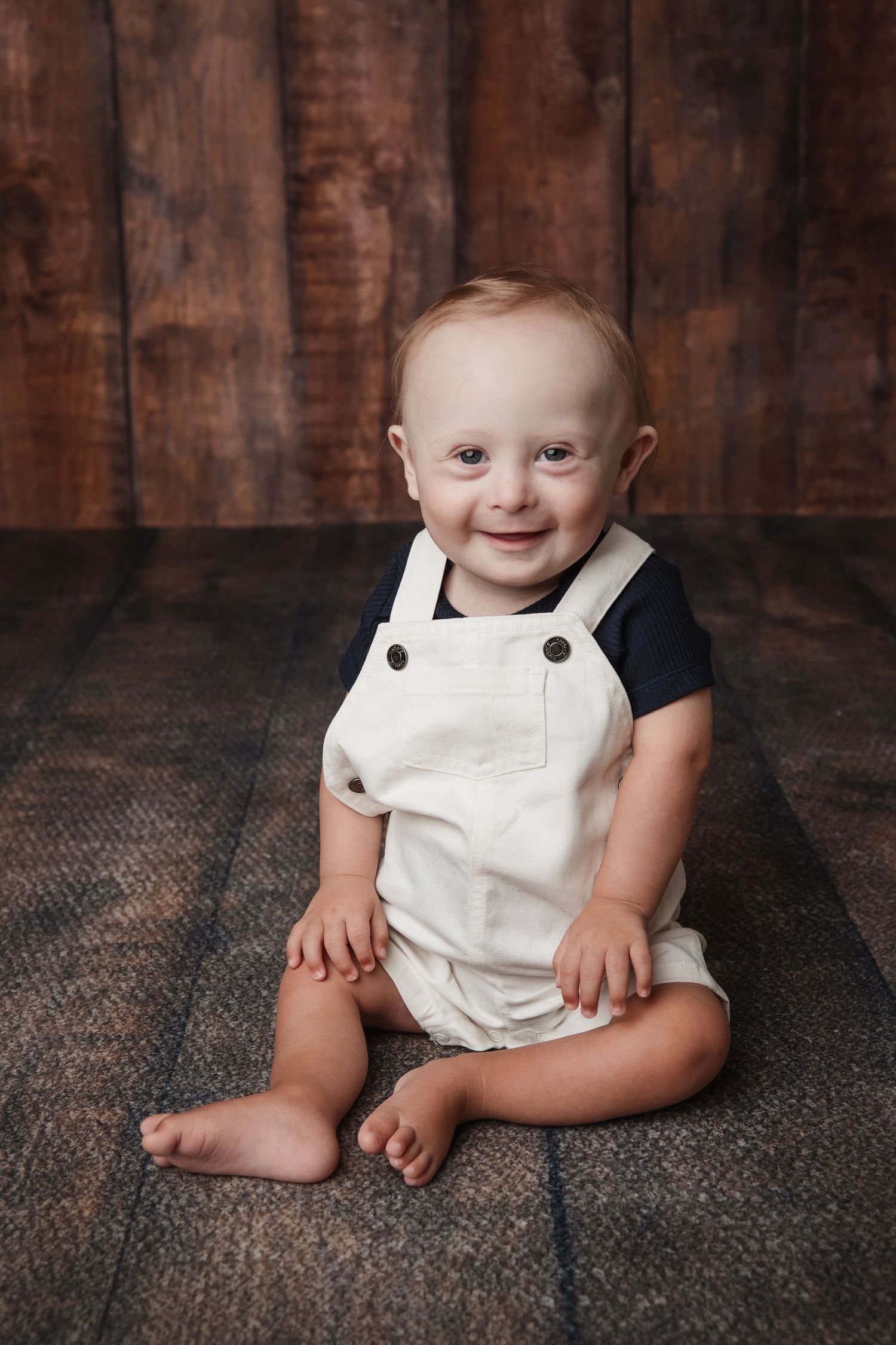 Progressive shots of a baby wearing white overalls seated on a textured brown surface.