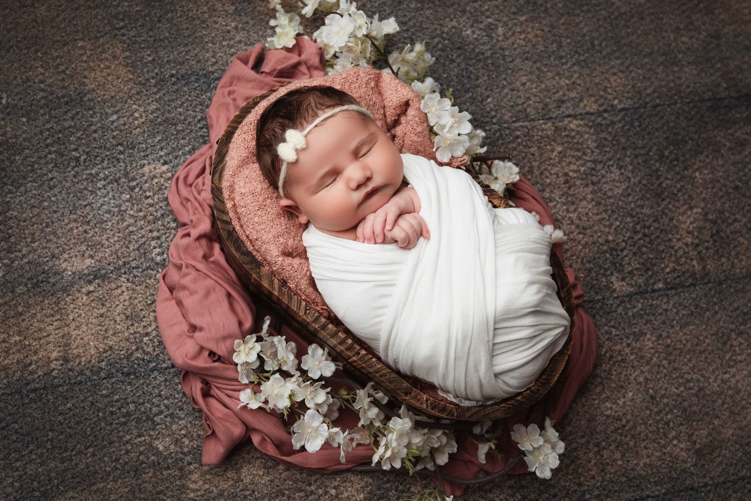 Artistic newborn portraits with baby wrapped in white against rustic backdrop with flowers.