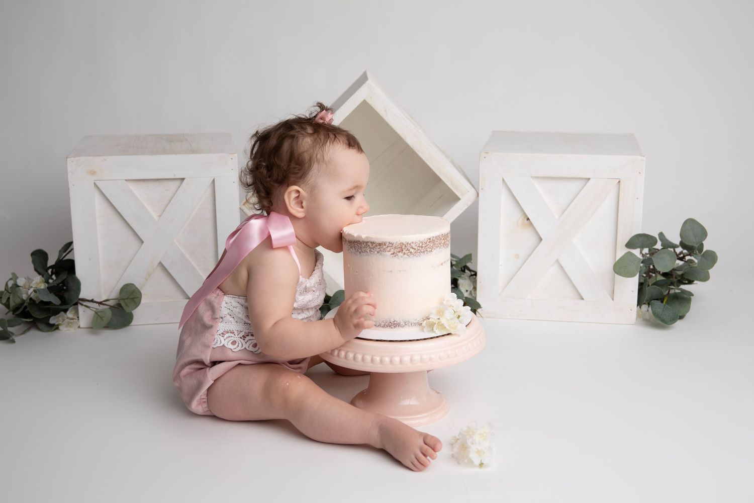 First birthday cake smash setup with geometric decorations and greenery on light grey background.